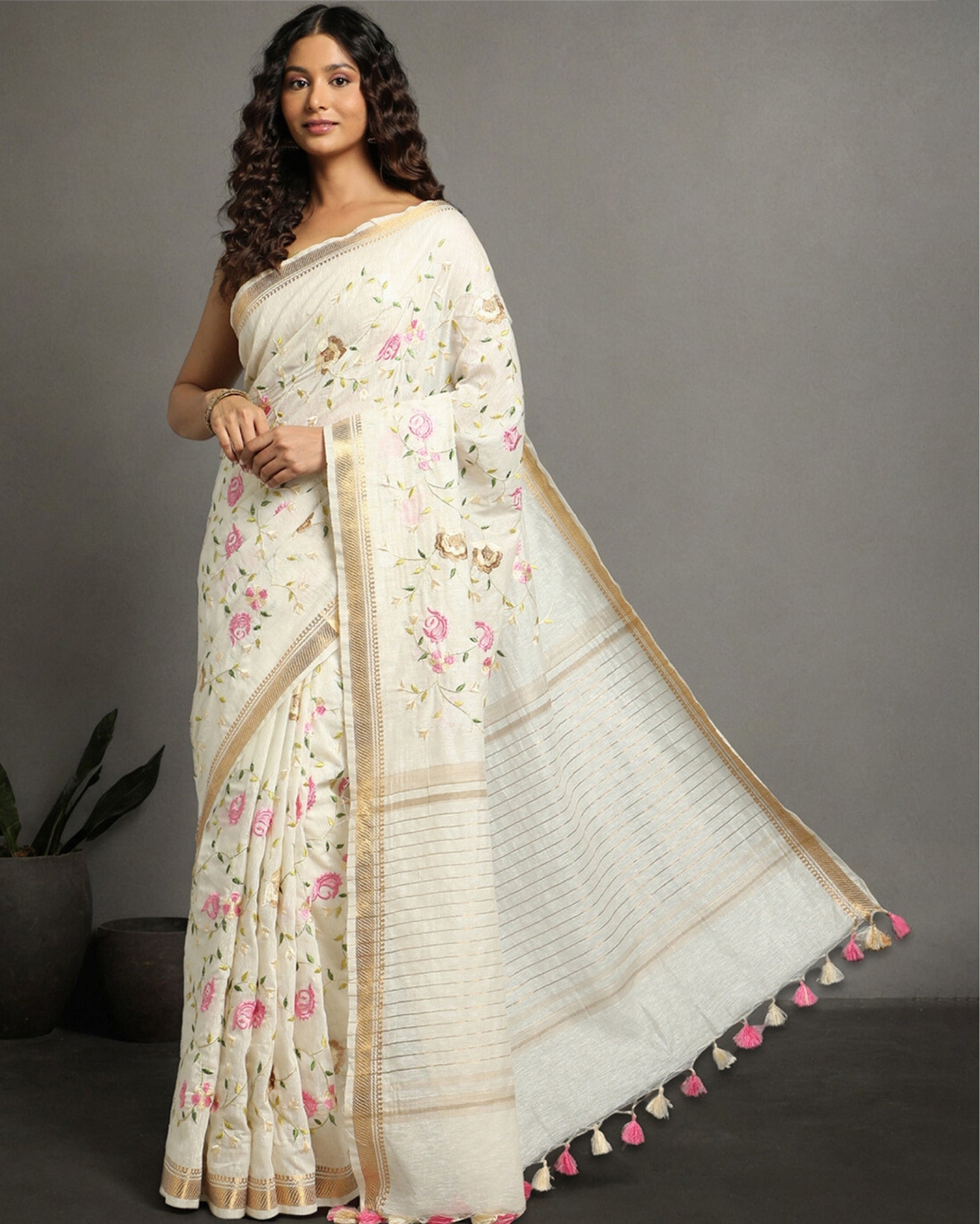 A model wearing an off-white silk linen embroidered saree with floral patterns and a beige border.