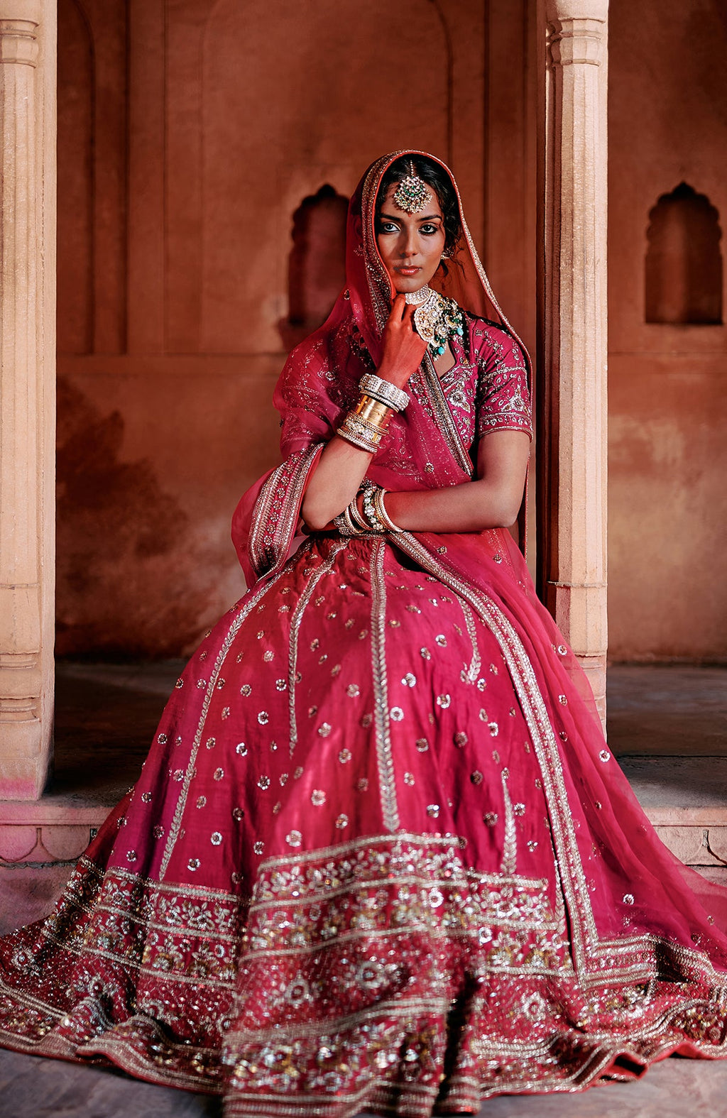 A woman in a red embroidered lehenga set with a matching dupatta and jewelry.