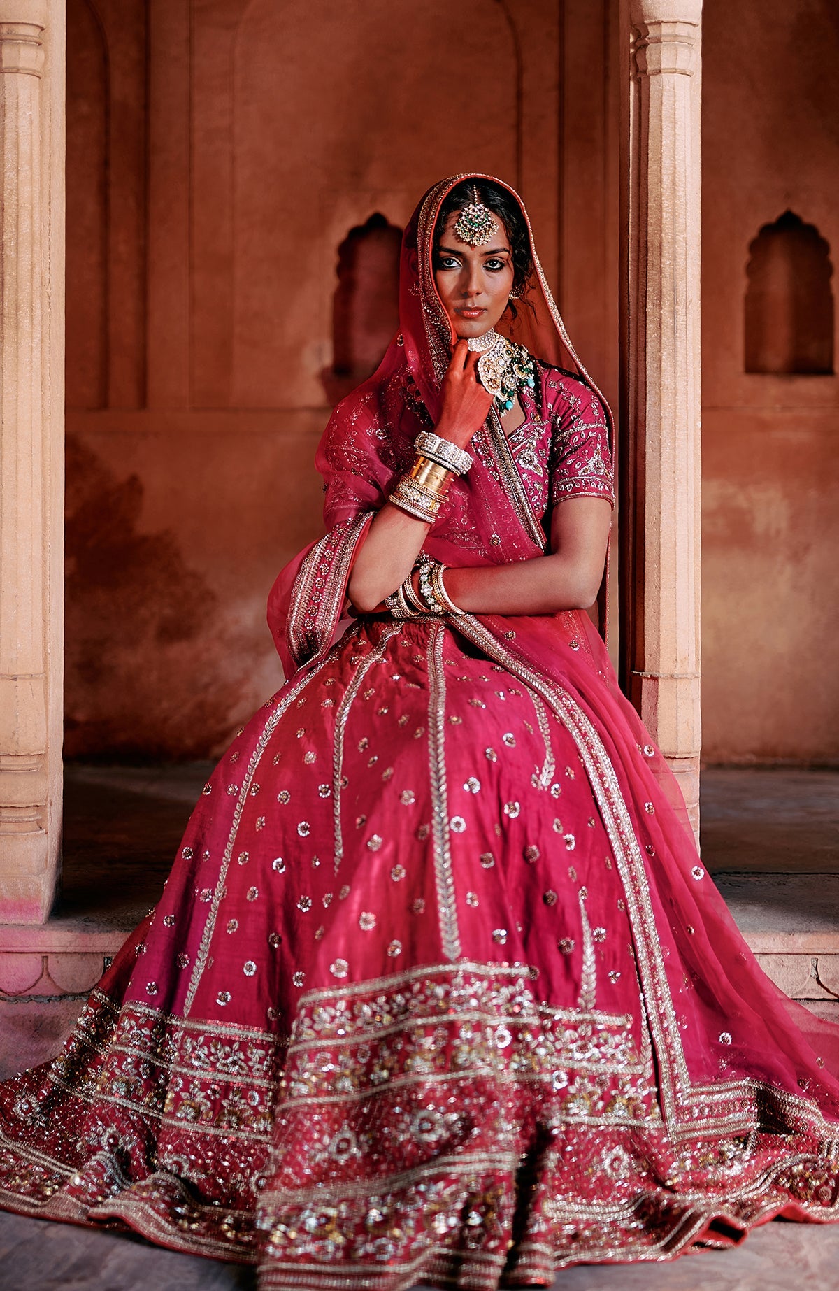 A woman in a red embroidered lehenga set with a matching dupatta and jewelry.