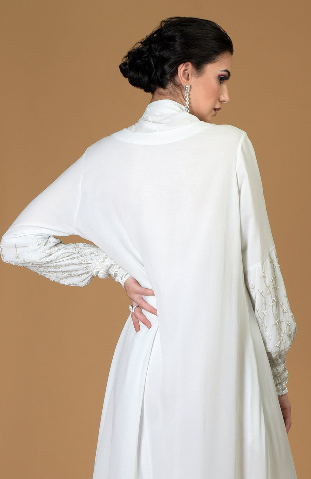 A woman models a white hand-embroidered dress with pearl and bead details on the sleeves.