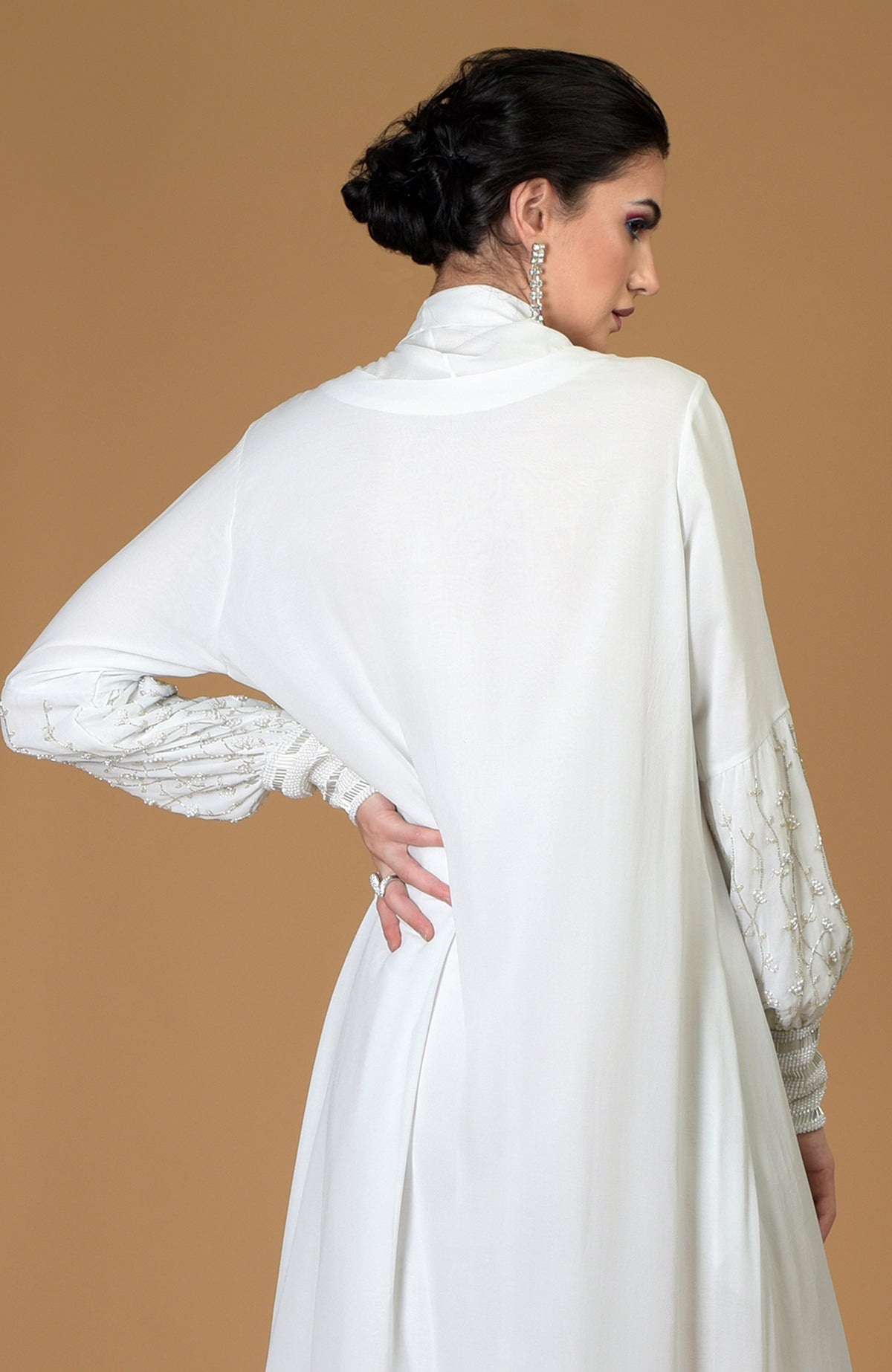 A woman models a white hand-embroidered dress with pearl and bead details on the sleeves.