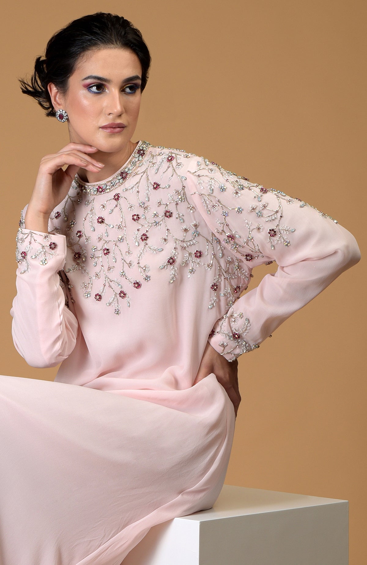 A woman models a pale pink dress with intricate crystal and bead embroidery.