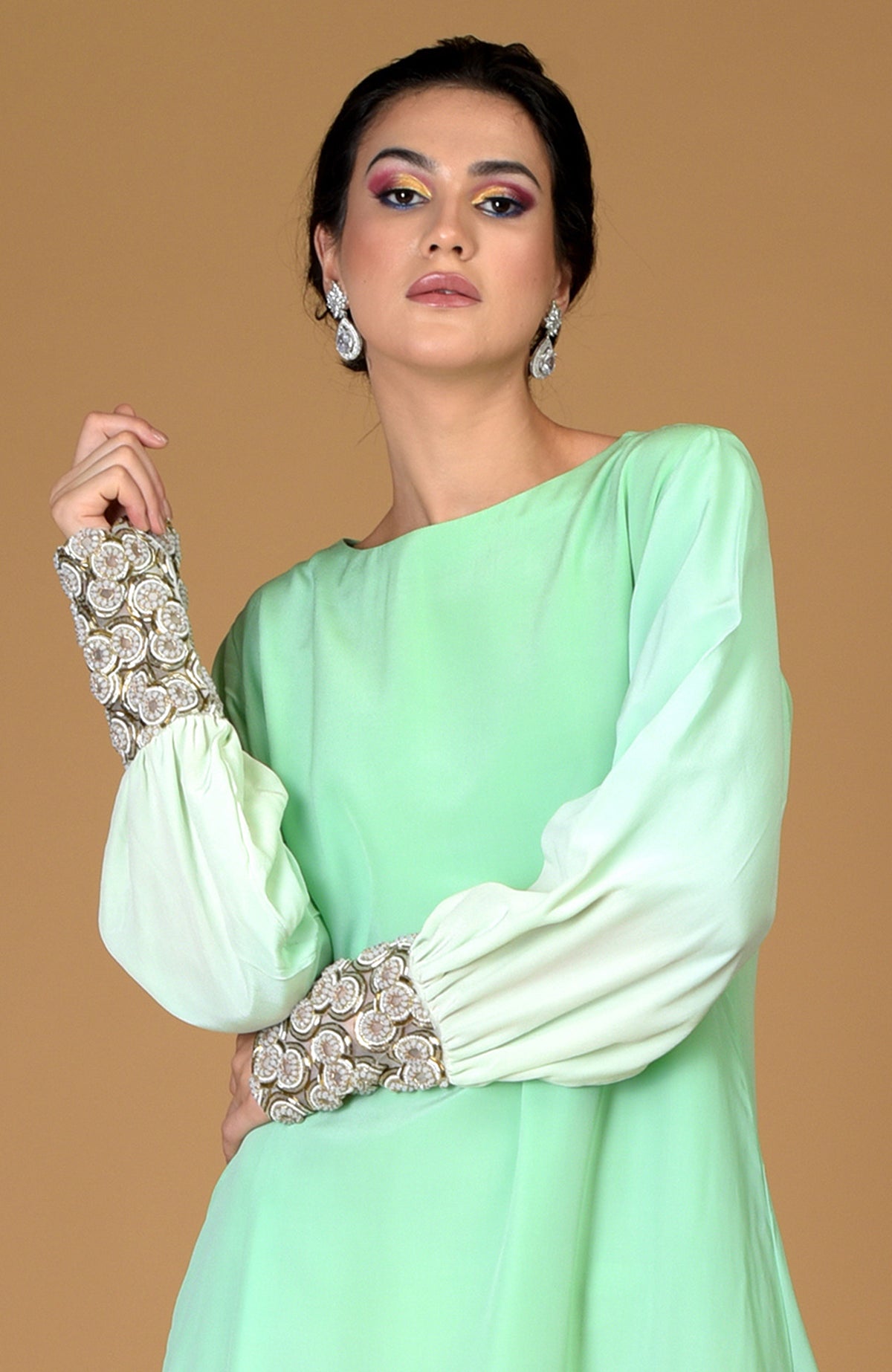 A woman models a sage green dress with sparkling circular jeweled cuffs.
