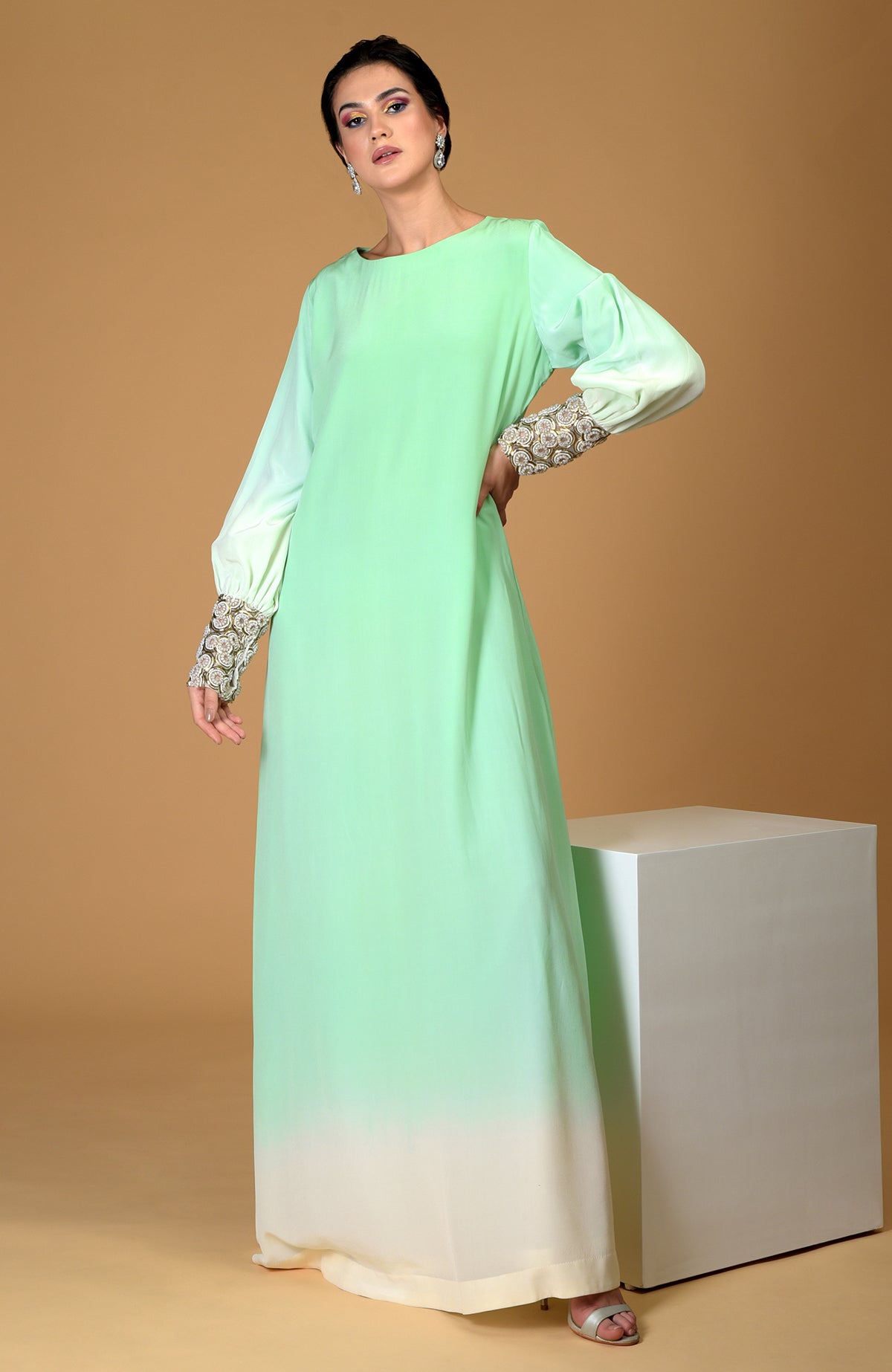 A woman models a sage green ombre silk crepe gown with sparkling jeweled cuffs.