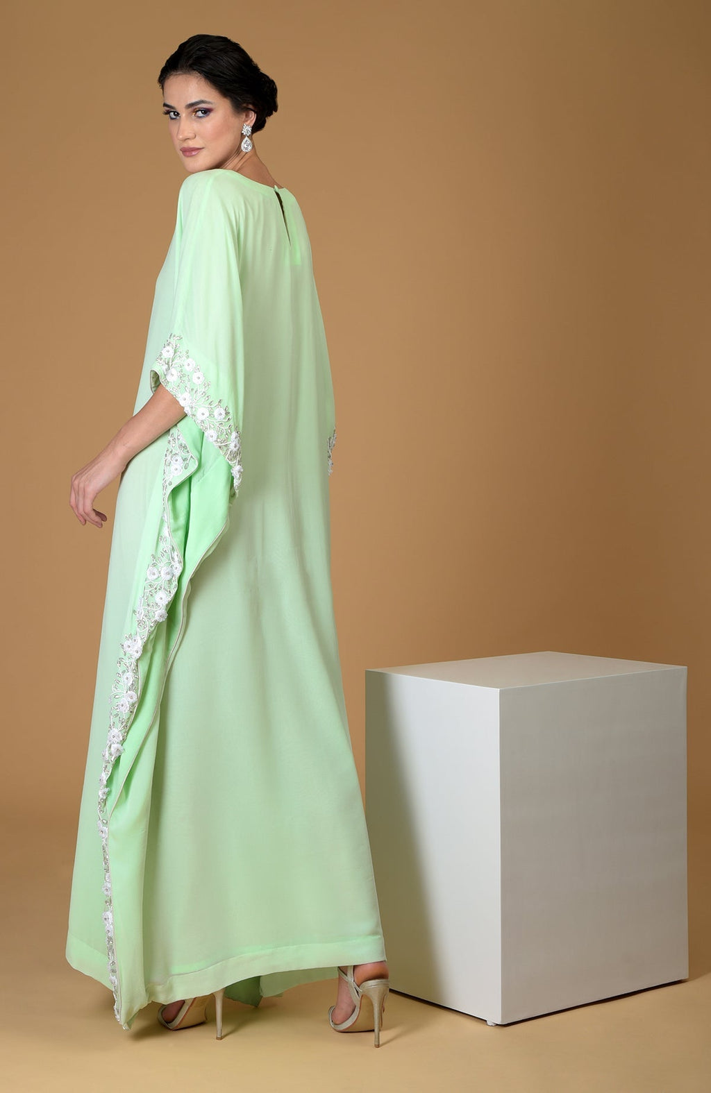 A woman in a mint green floral hand-embroidered kaftan dress and heels.