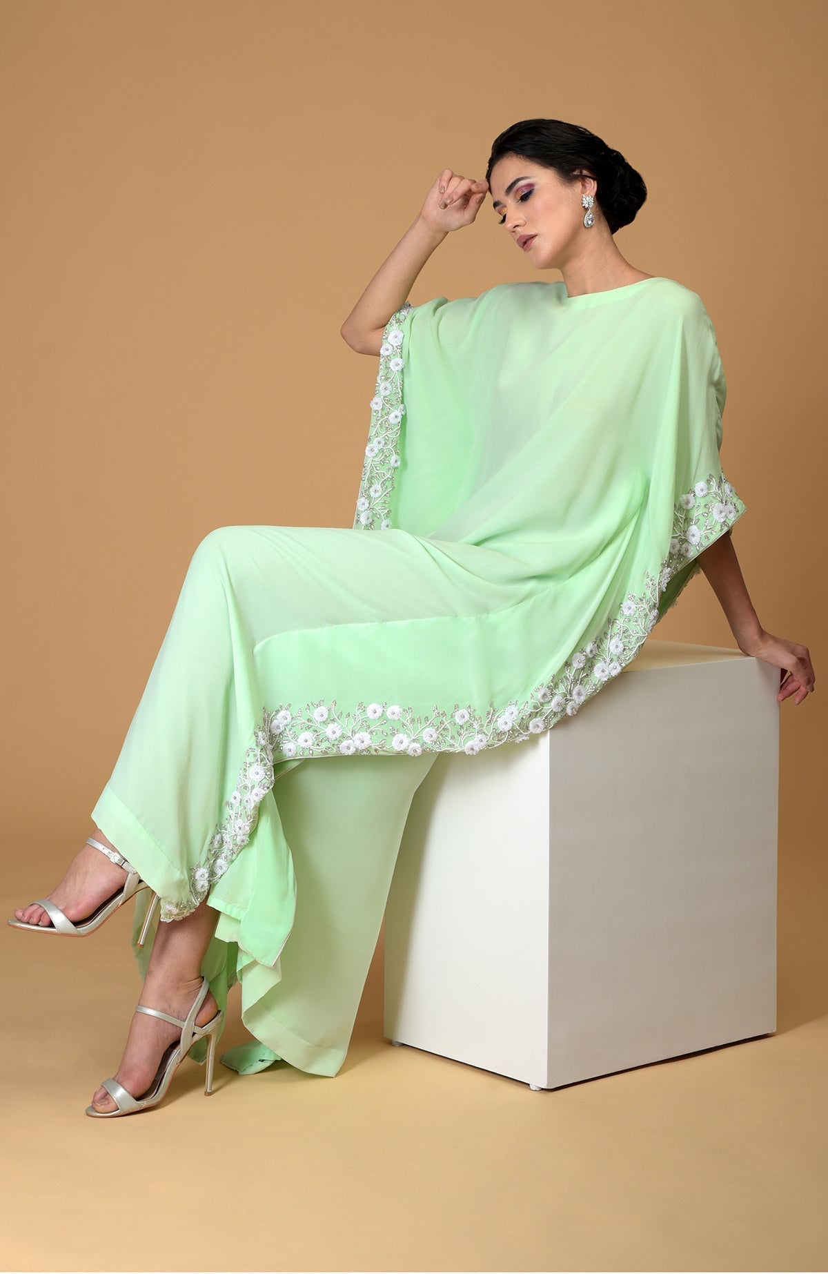 A woman models a mint green kaftan dress with white floral embroidery.