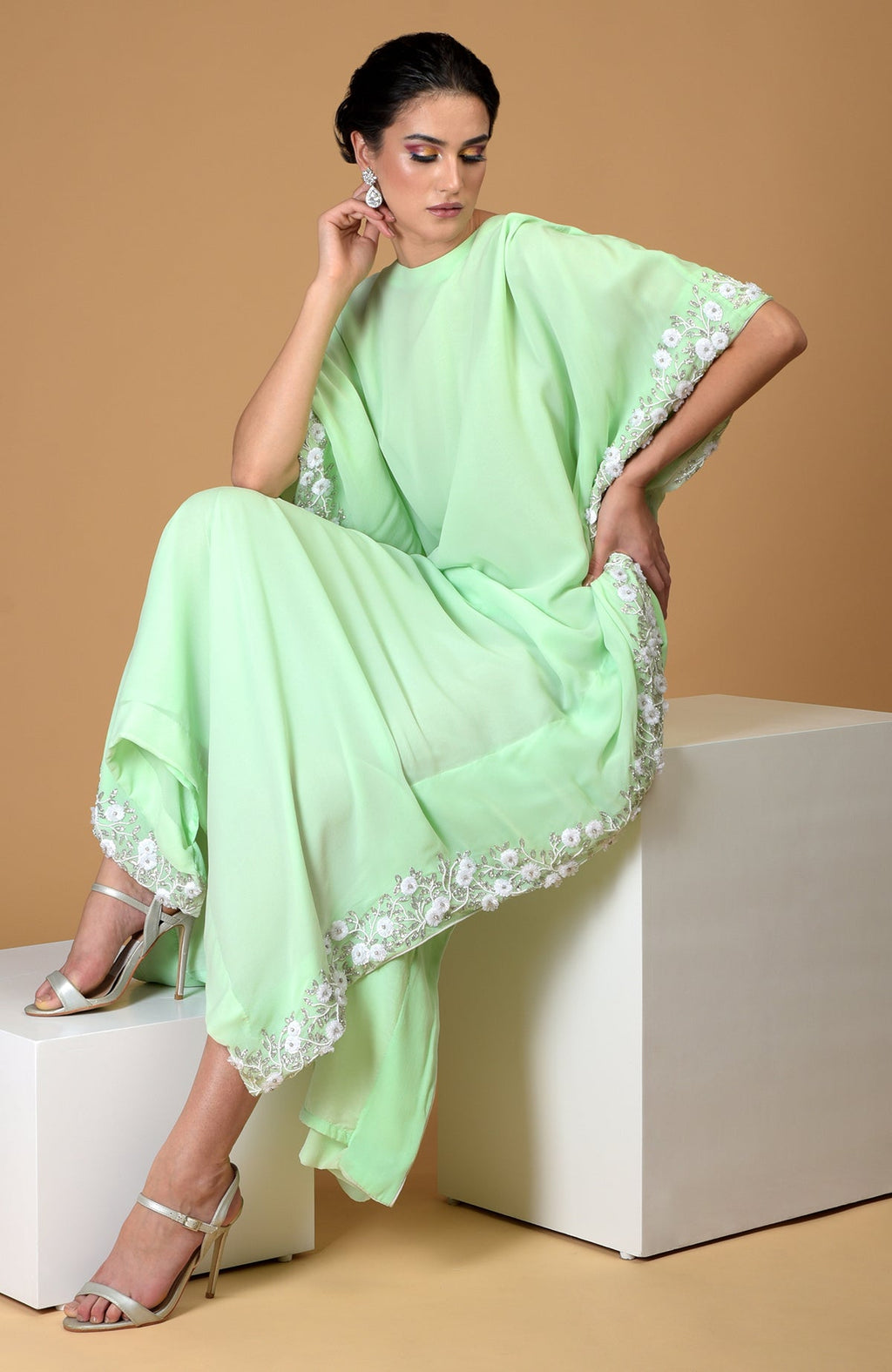 A woman models a mint green floral hand-embroidered dress with silver heels.