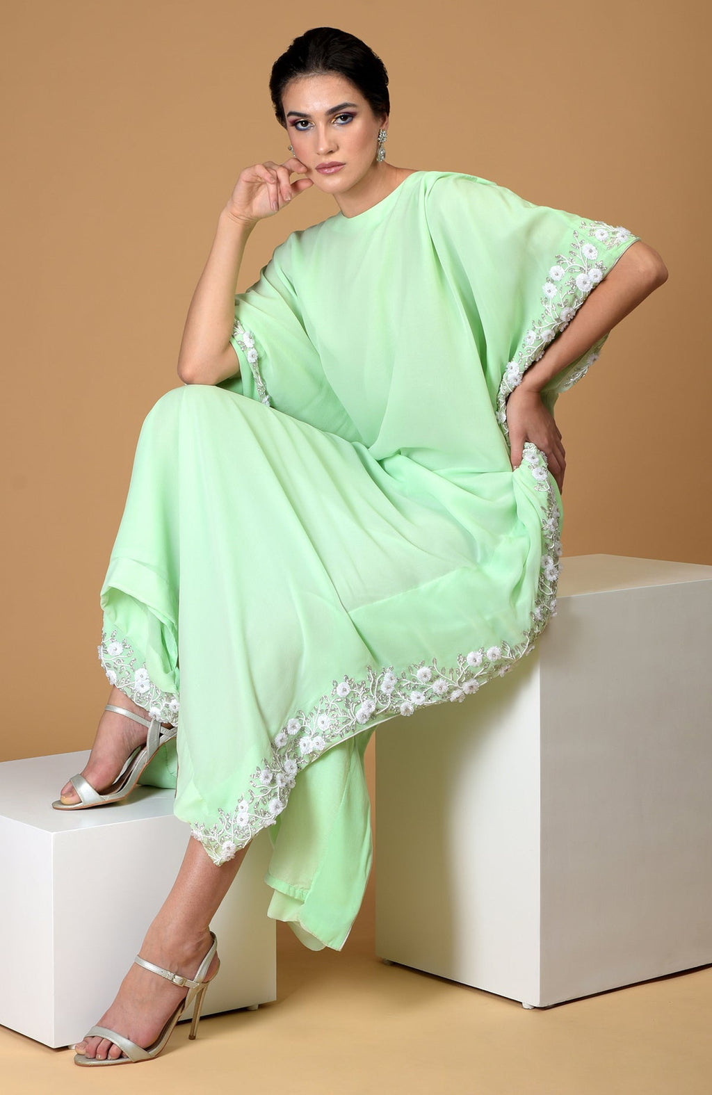 A woman models a mint green kaftan dress with white floral embroidery.