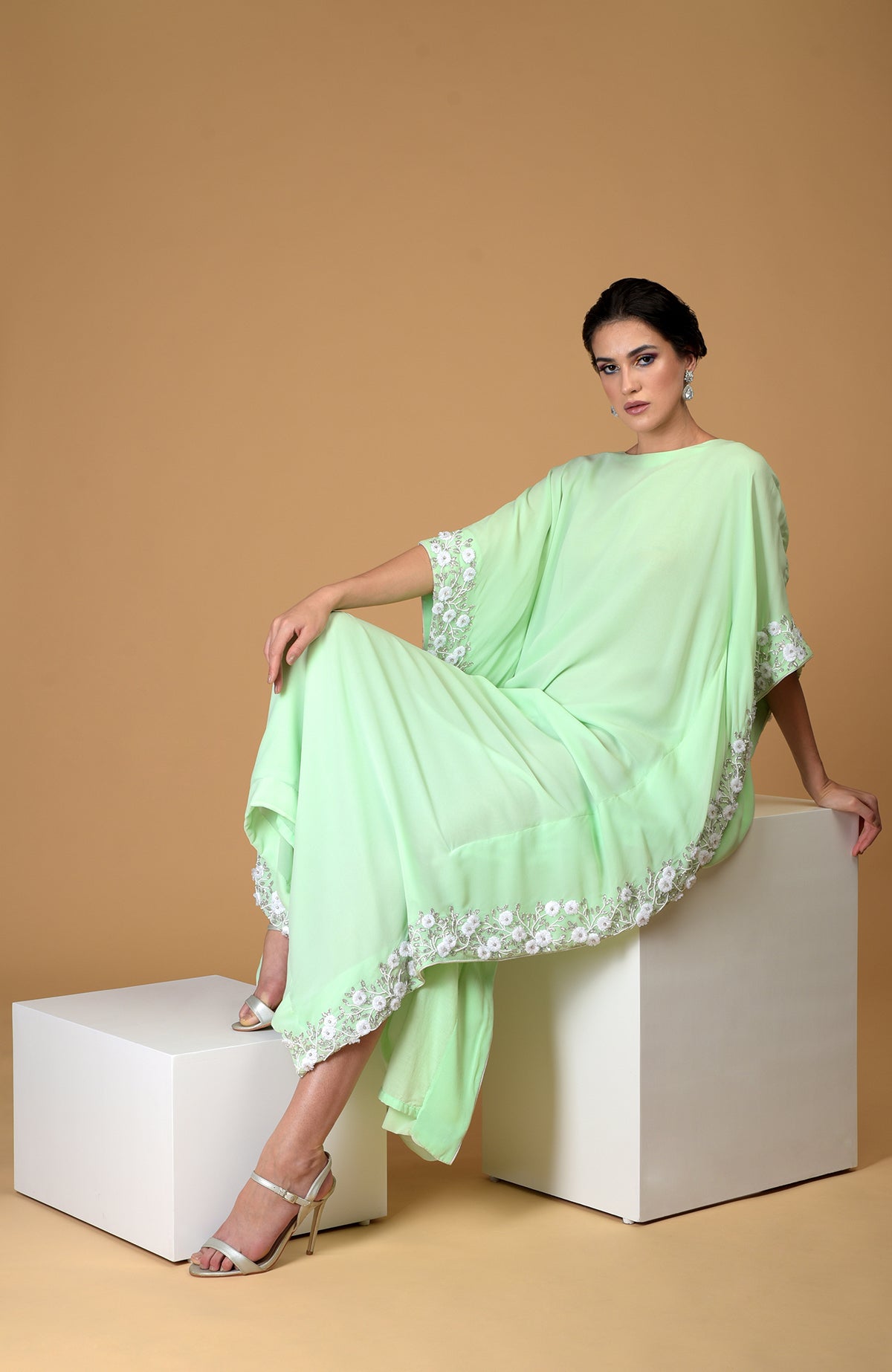A woman models a mint green floral hand-embroidered kaftan dress with white heels.
