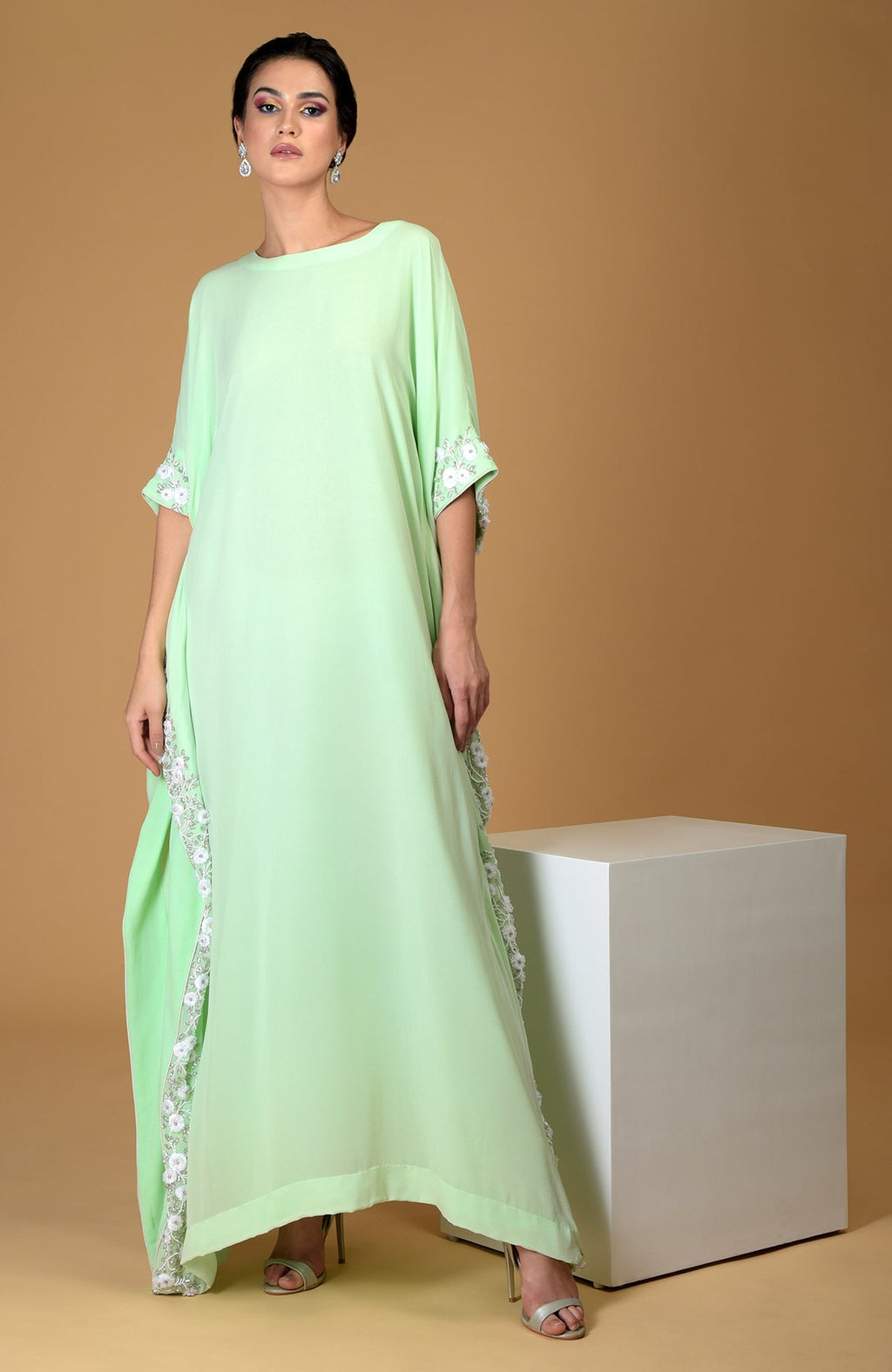A woman models a mint green kaftan dress with white floral embroidery.