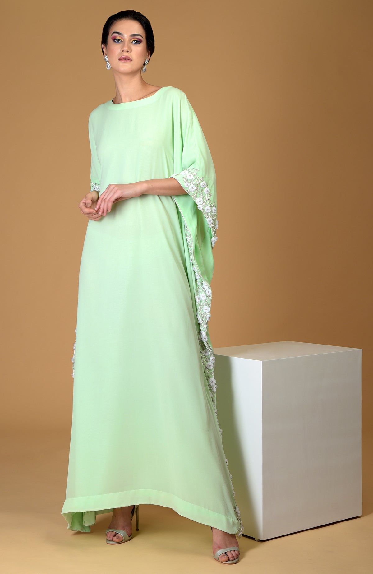 A woman models a mint green floral hand-embroidered kaftan dress.