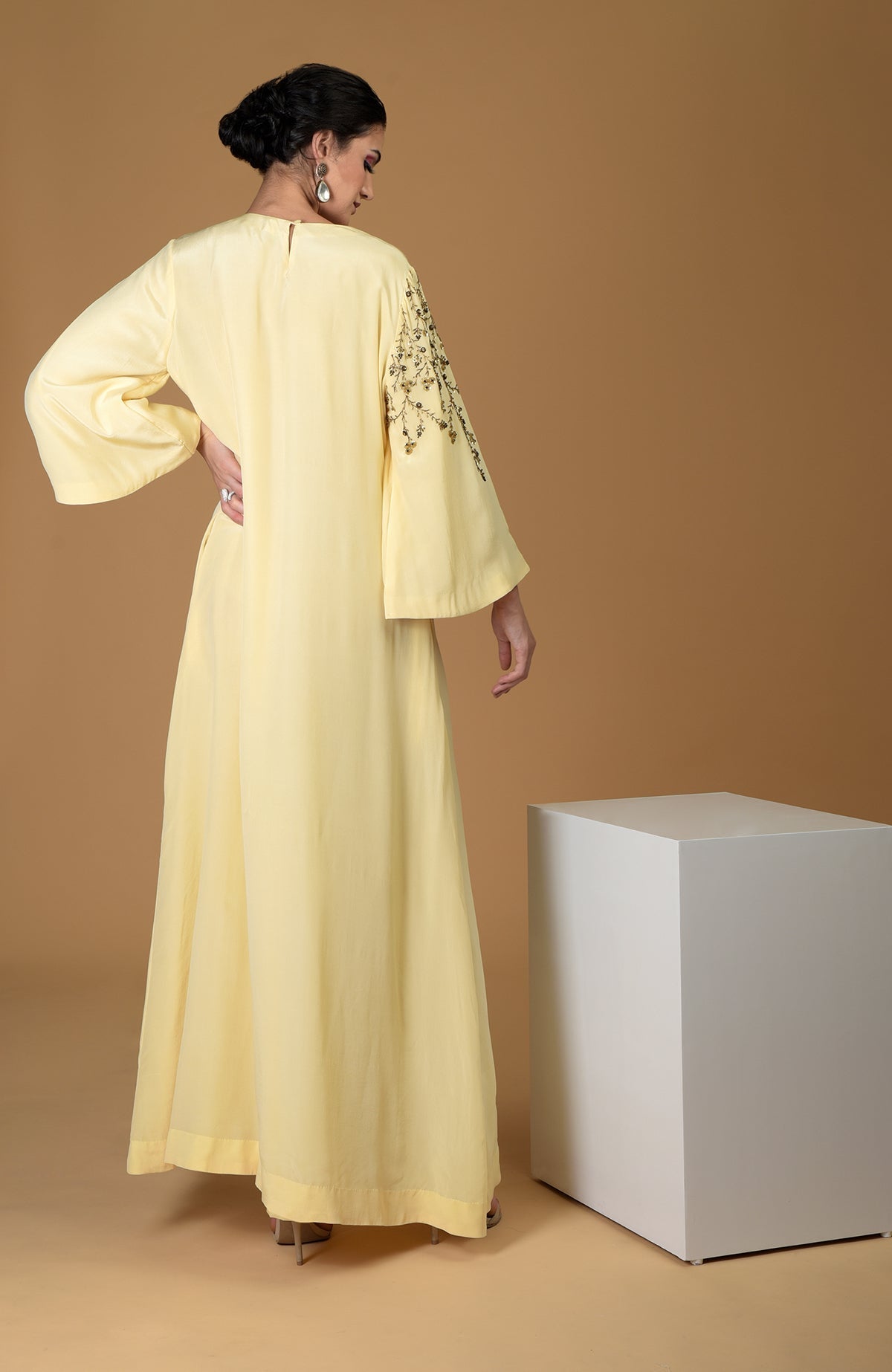 A woman models a lemon yellow dress with dainty floral embroidery on one sleeve.