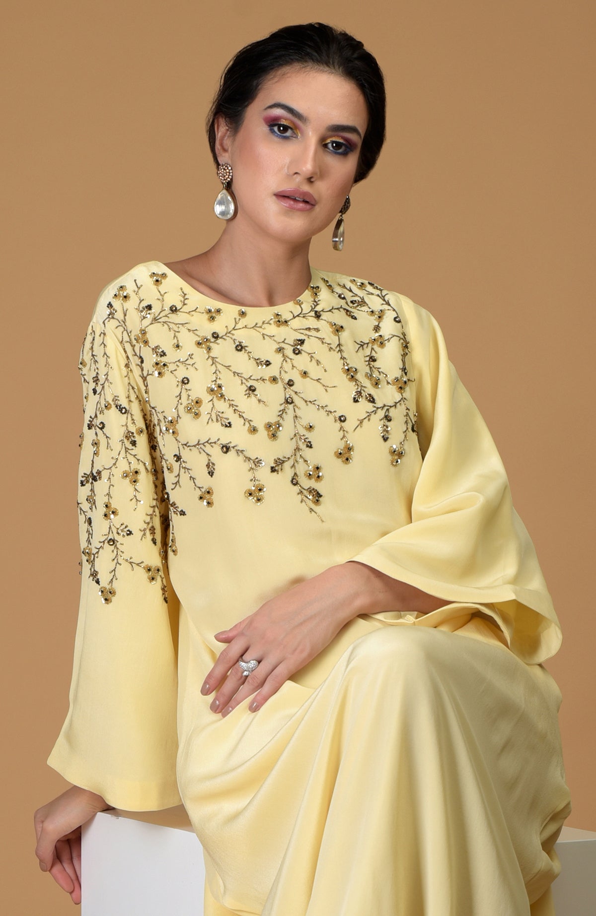 A woman models a lemon yellow dress with dainty floral embroidery and bell sleeves.