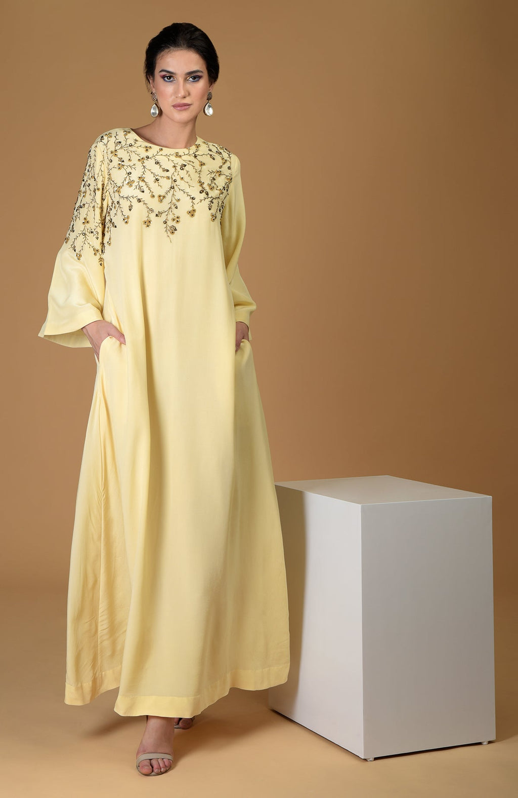 A woman models a lemon yellow dress with dainty floral embroidery and pockets.