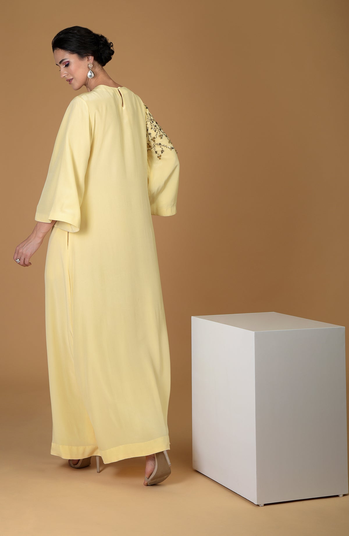 A woman models a lemon yellow dress with floral embroidery on the sleeve.