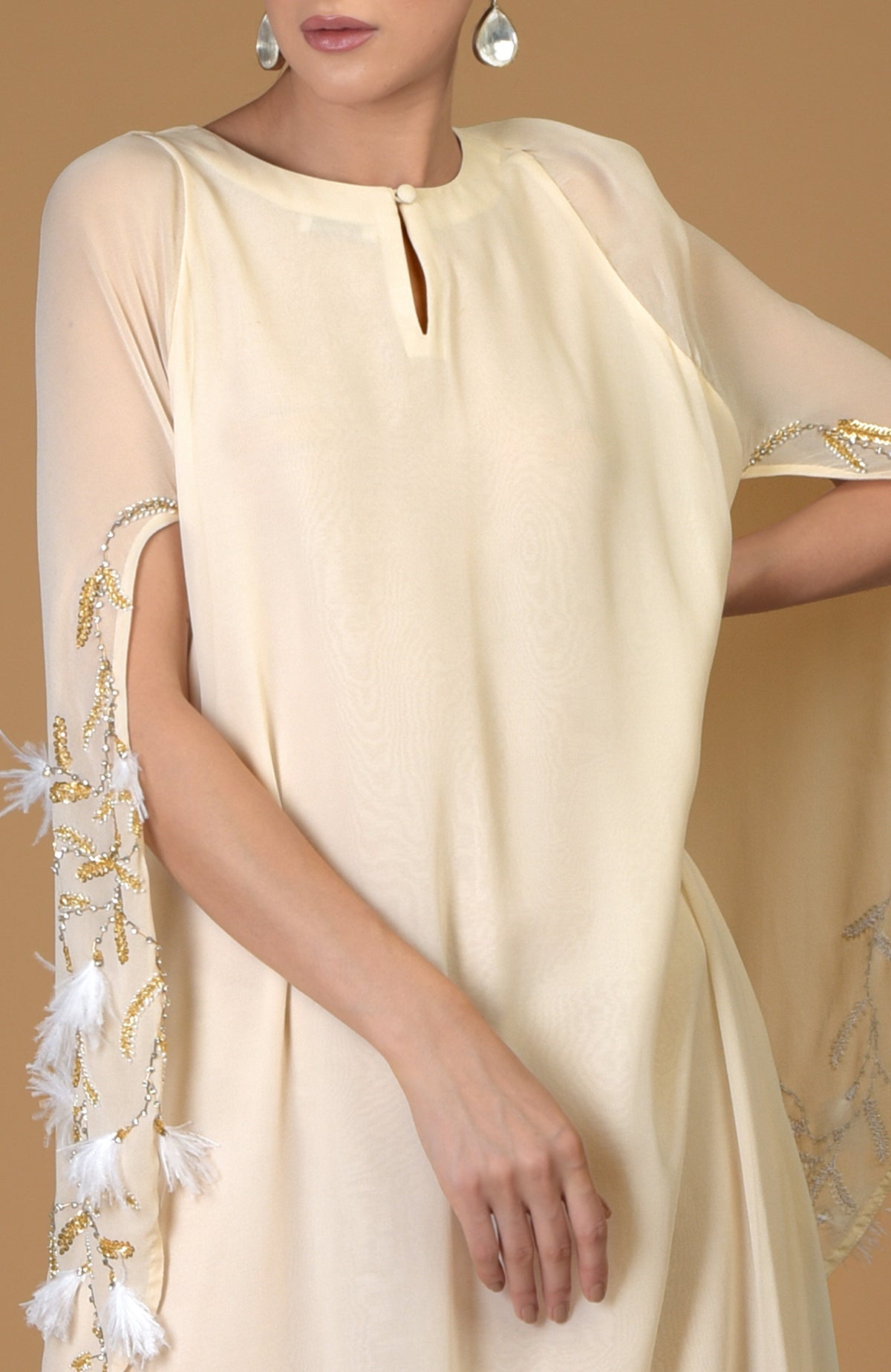 A woman models a cream-colored dress with embroidered and feathered sleeves.