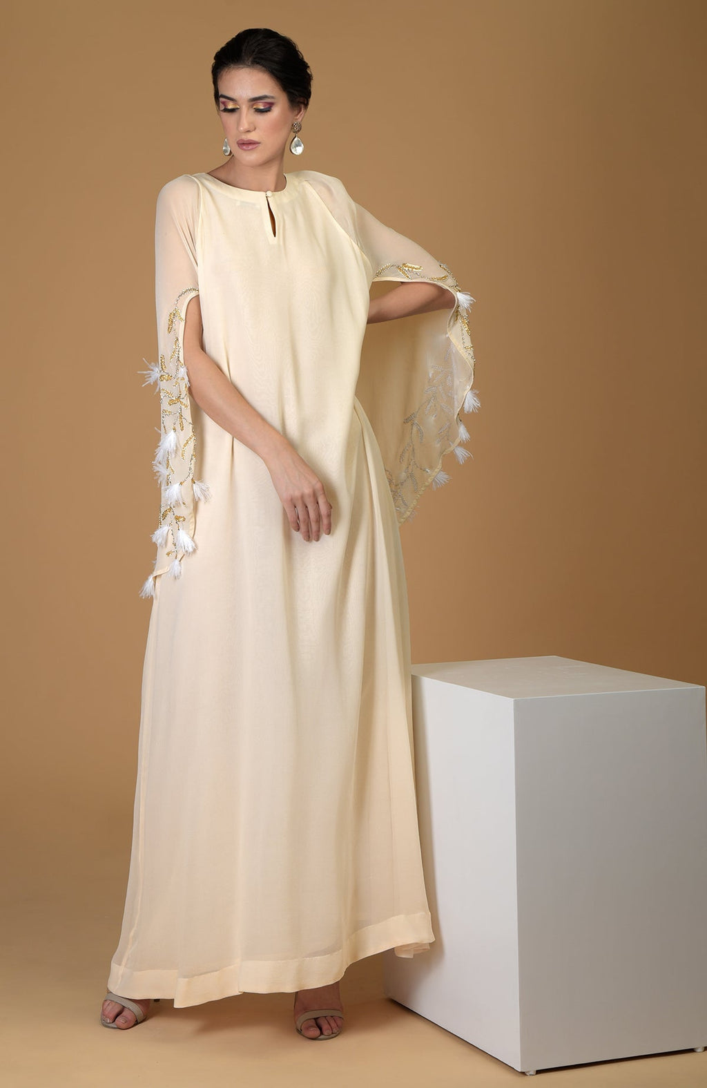 A woman models a cream-colored cape dress with gold and white feather embroidery.