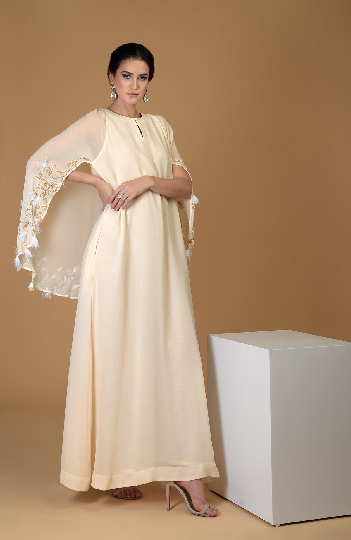 A woman models a cream-colored dress with a sheer, embroidered cape.