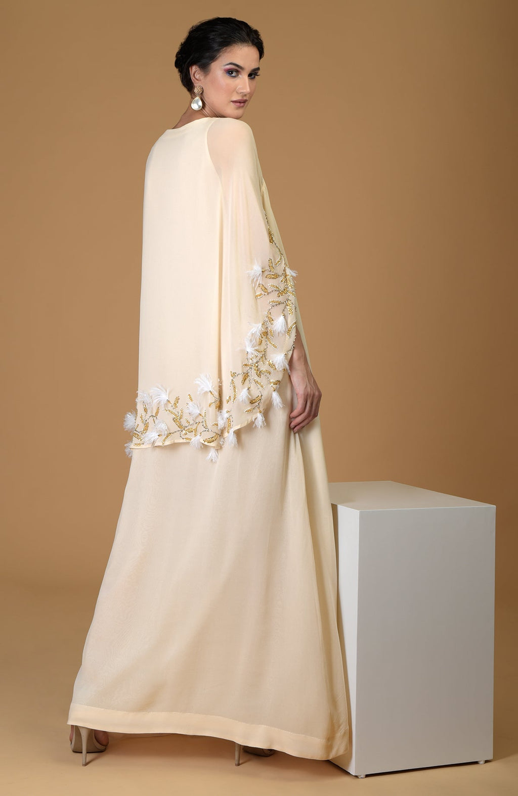 Bloom Cape Hand Embroidered Dress in a light color with feather and gold embellishments.