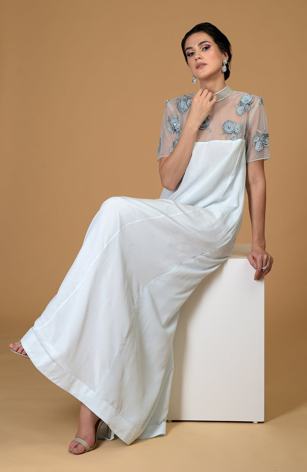 A woman sits wearing a light blue dress with an embroidered sheer top.
