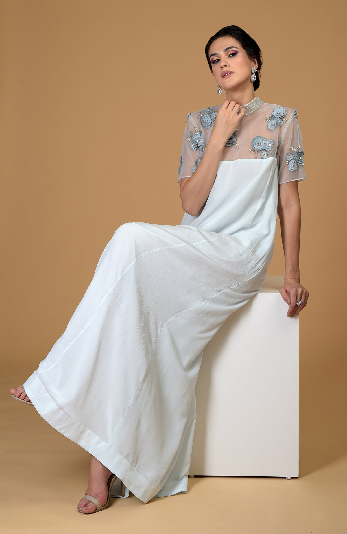 A woman sits wearing a light blue dress with an embroidered sheer top.
