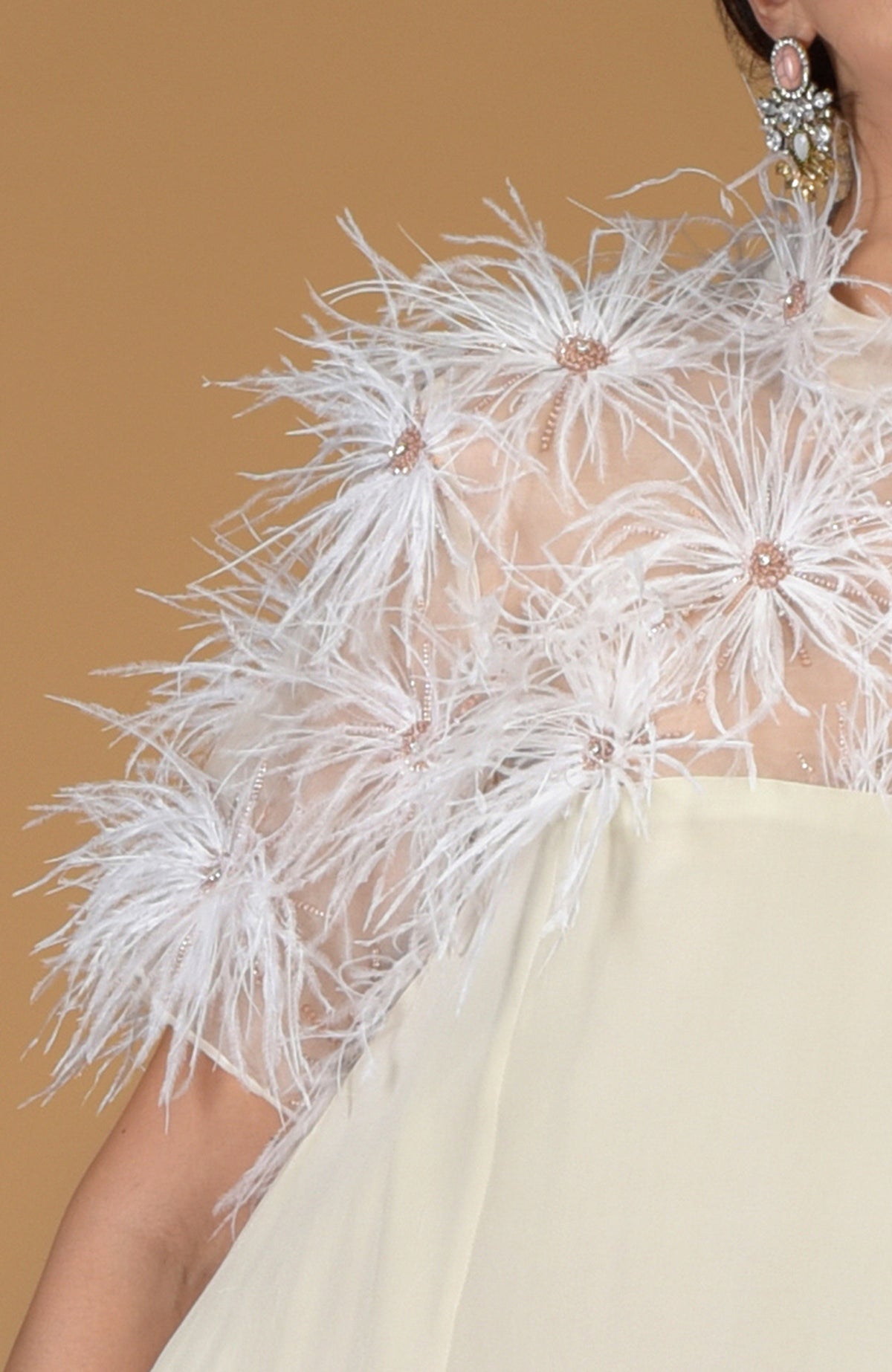 An off-white dress features a sheer top adorned with white feather flowers and delicate beading.
