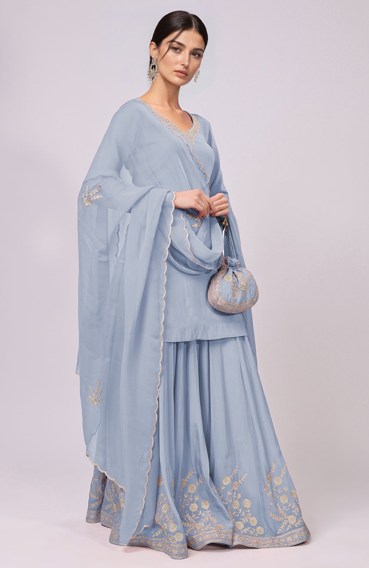A woman models a dusty blue Kashmiri Tilla Aari embroidered sharara set with a matching potli bag.
