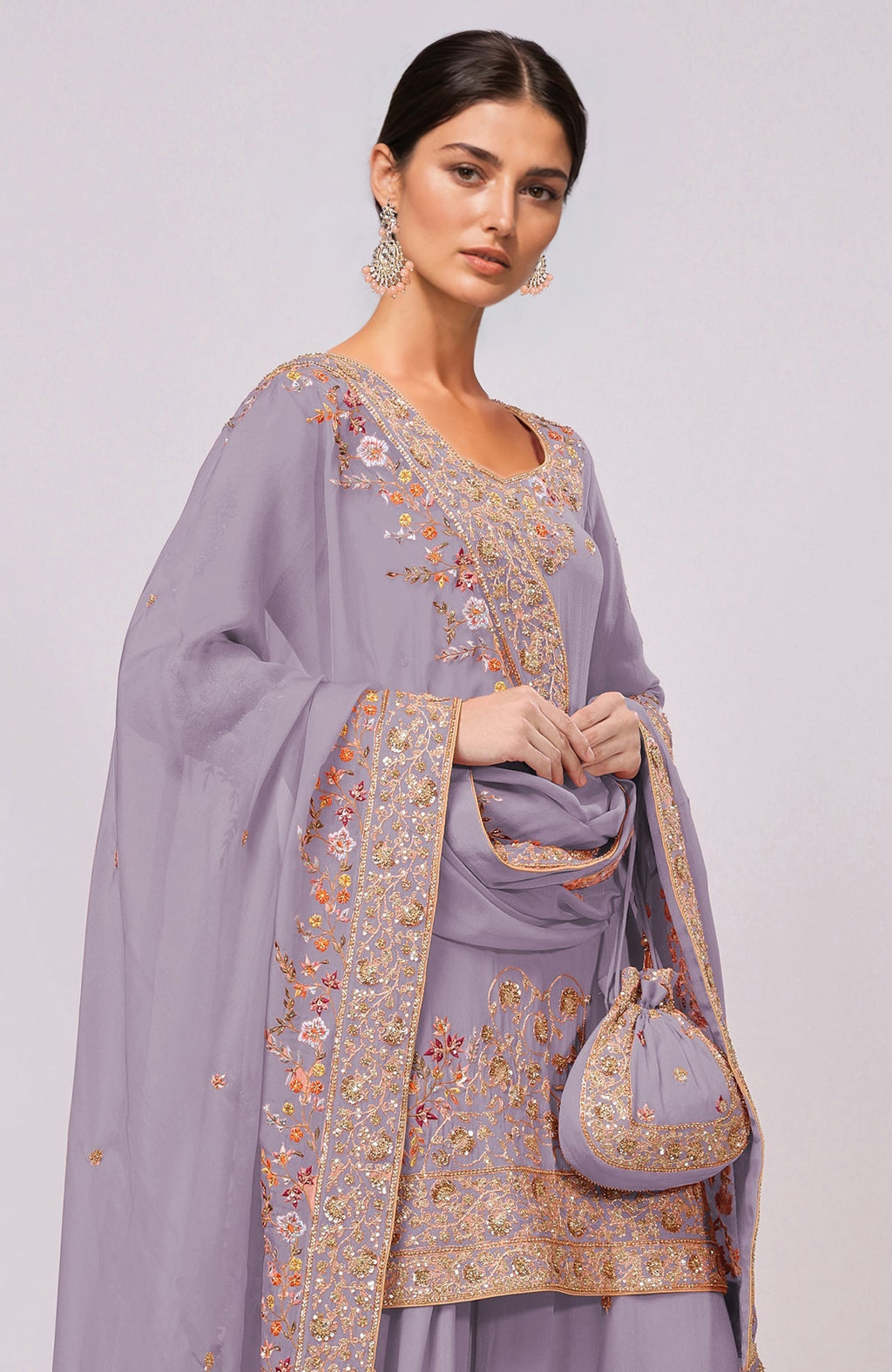 A woman models an elderberry sharara set with gold and resham embroidery and a matching potli bag.