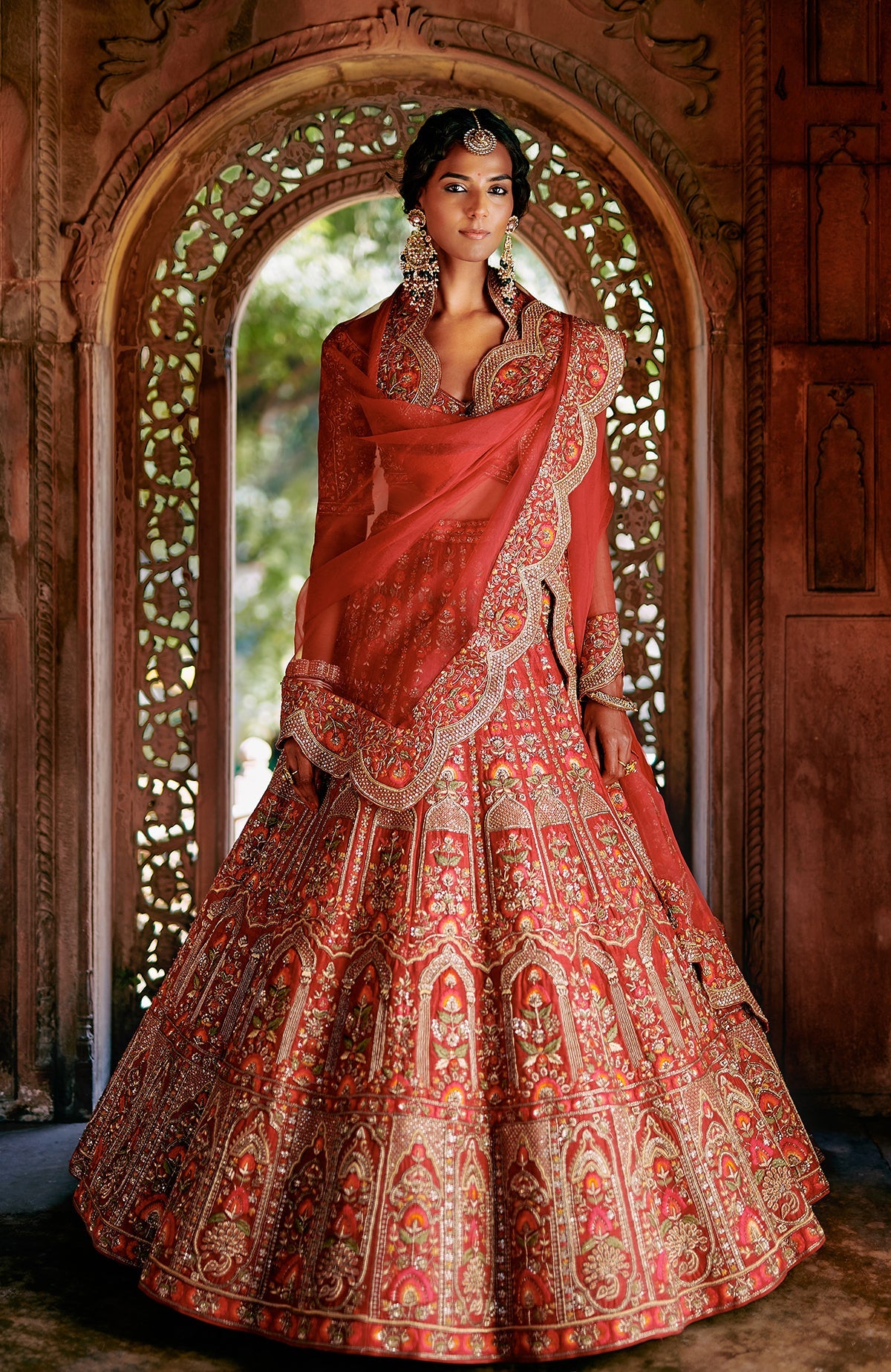 Red lehenga set with intricate gold embroidery, floral motifs, peacock tassels, and sheer dupatta.