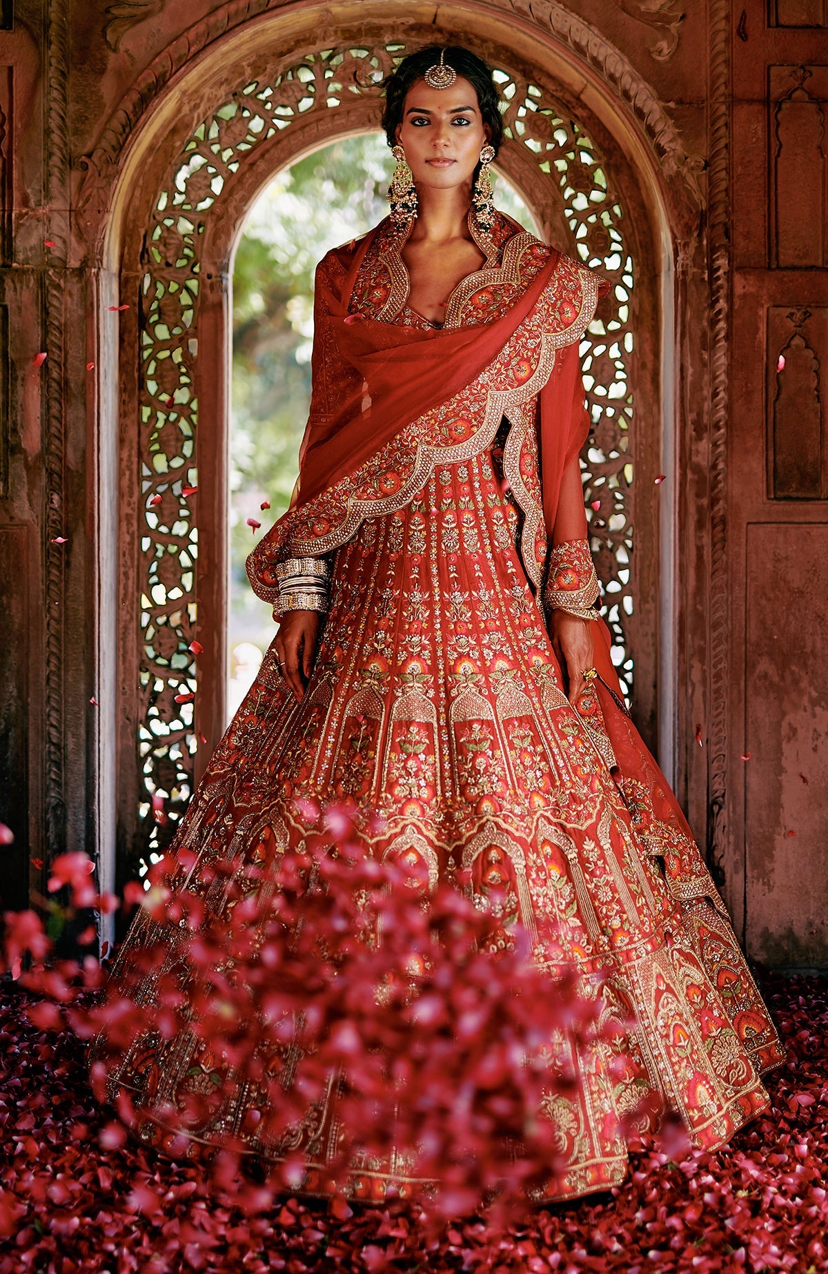 Red lehenga set with intricate floral embroidery, gold detailing, peacock tassels, and scalloped dupatta.