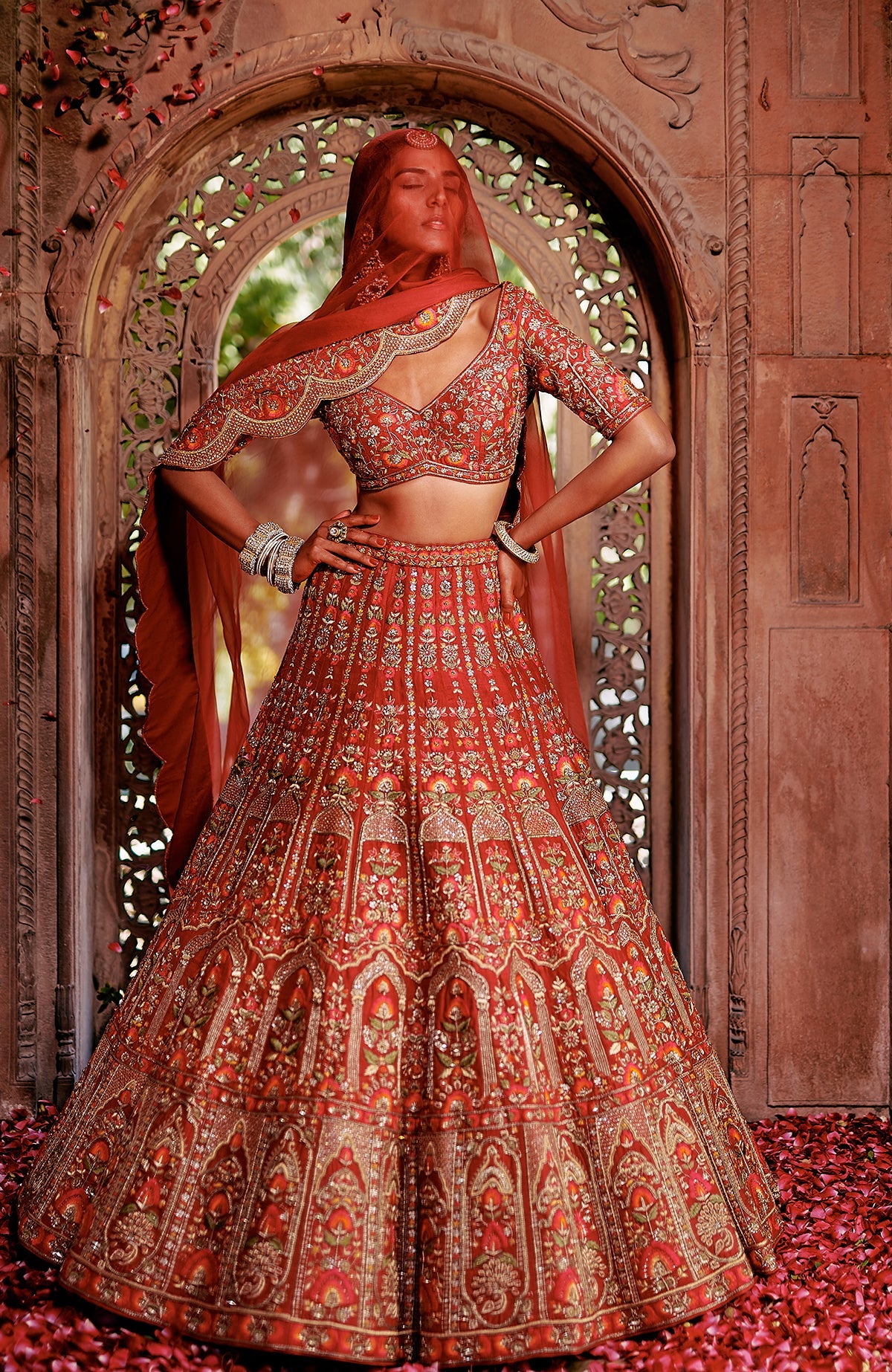 Red lehenga set with intricate floral embroidery, gold zari work, peacock tassels, and scalloped dupatta.