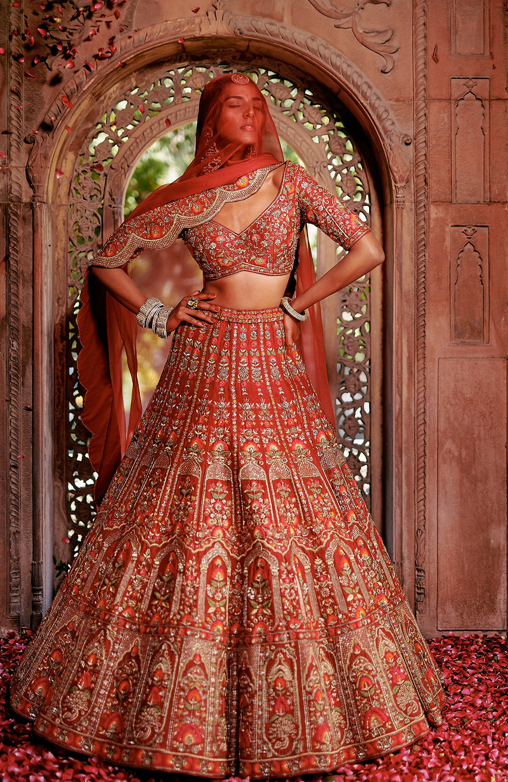 Red lehenga set with intricate floral embroidery, gold zari work, peacock tassels, and scalloped dupatta.