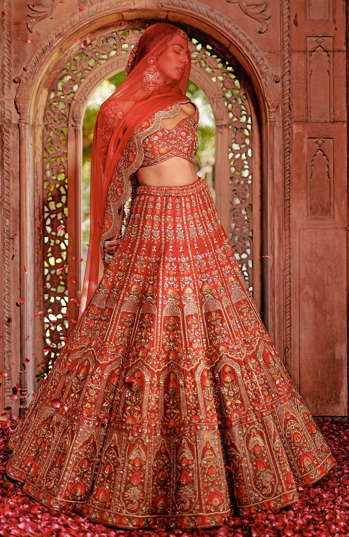 Red lehenga set with intricate gold embroidery, peacock tassels, and a sheer scalloped dupatta.