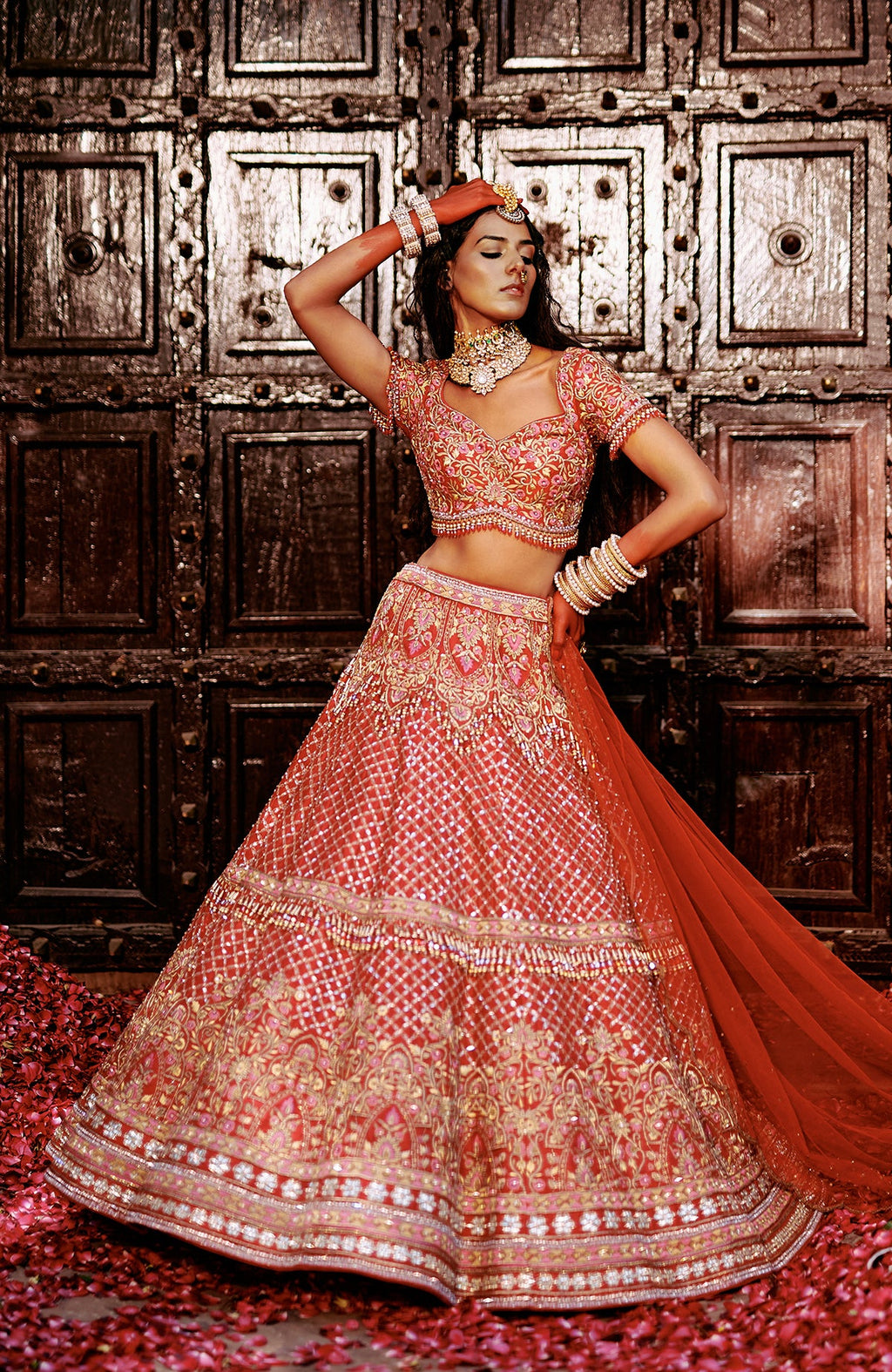 Red lehenga set with pink and gold floral embroidery, crystal accents, tassels, and sheer dupatta.