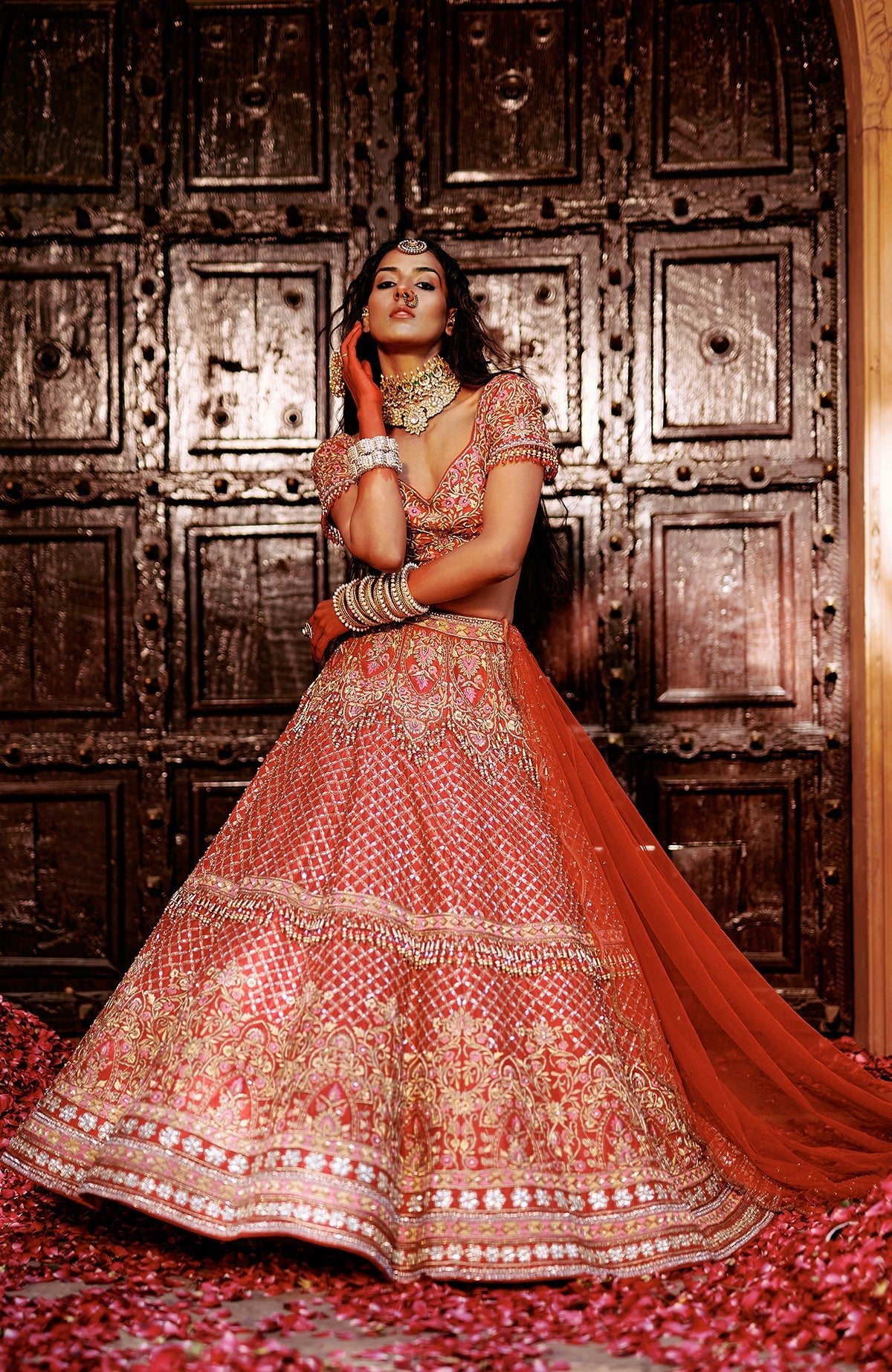 Red lehenga set with intricate pink and gold embroidery, crystal embellishments, and peacock tassels.