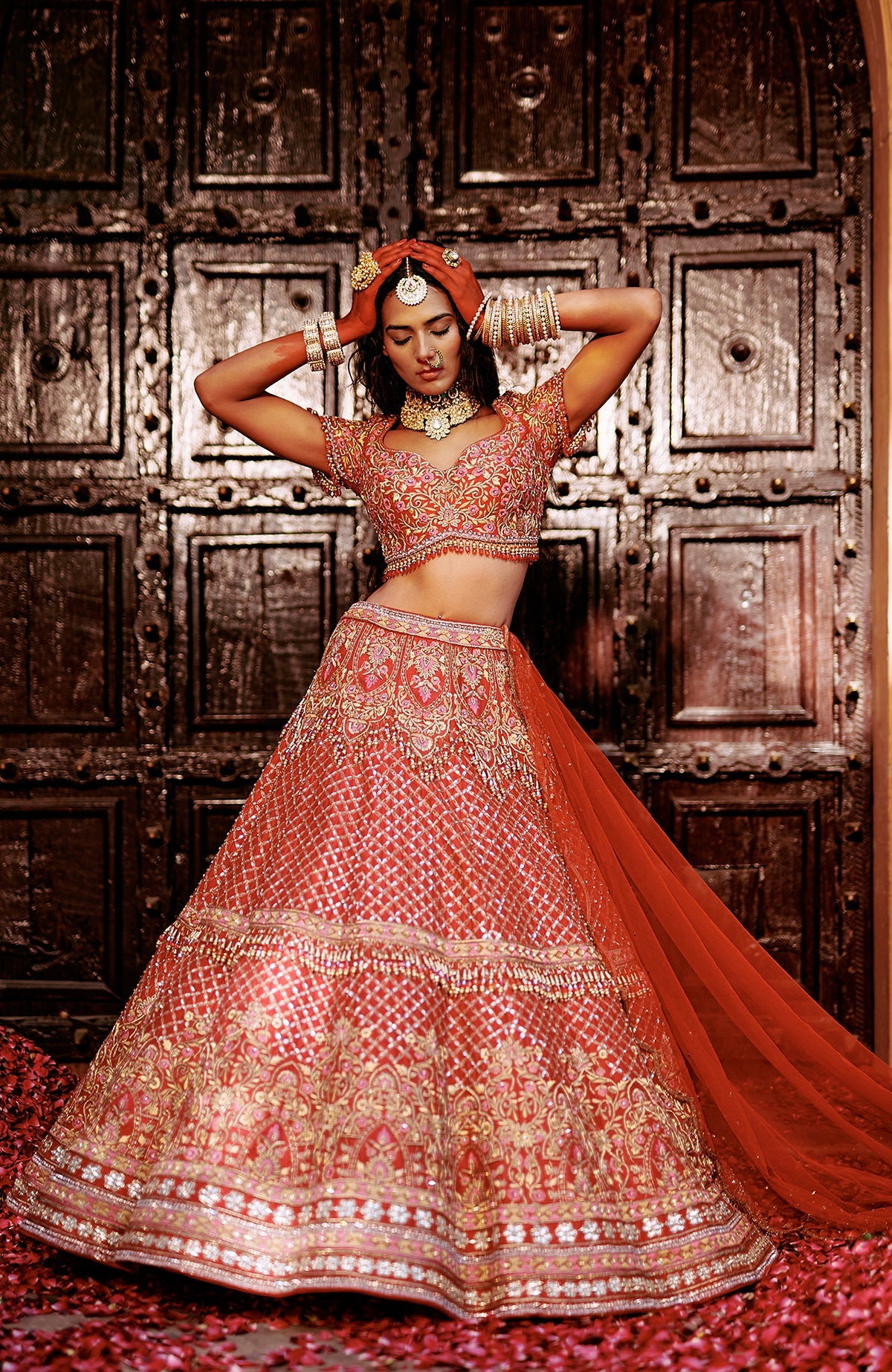 Red lehenga set with gold and pink floral embroidery, crystal accents, tassels, and sheer dupatta.