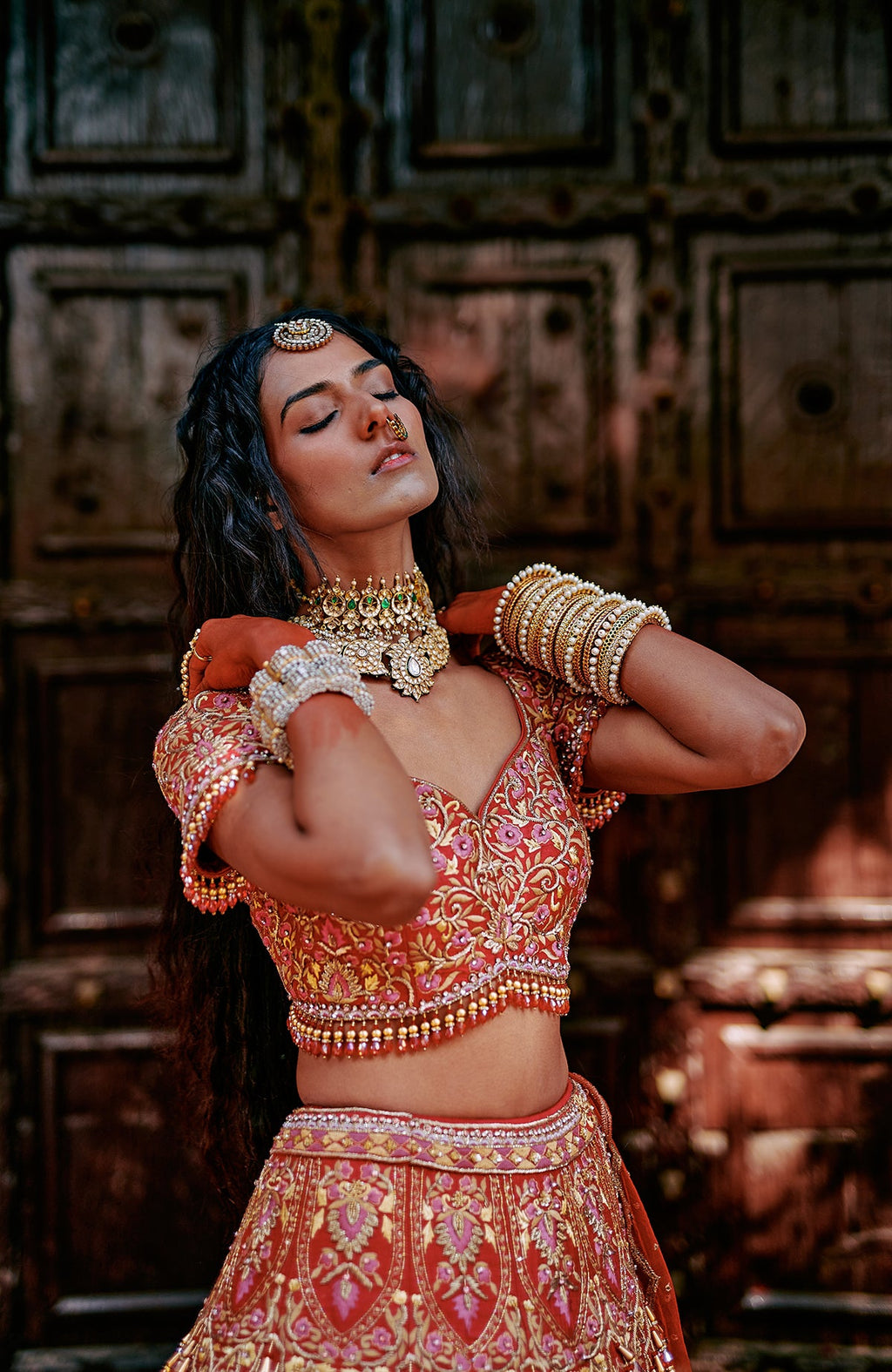 Red lehenga set with pink and gold floral embroidery, crystal accents, tassels, and sheer dupatta.