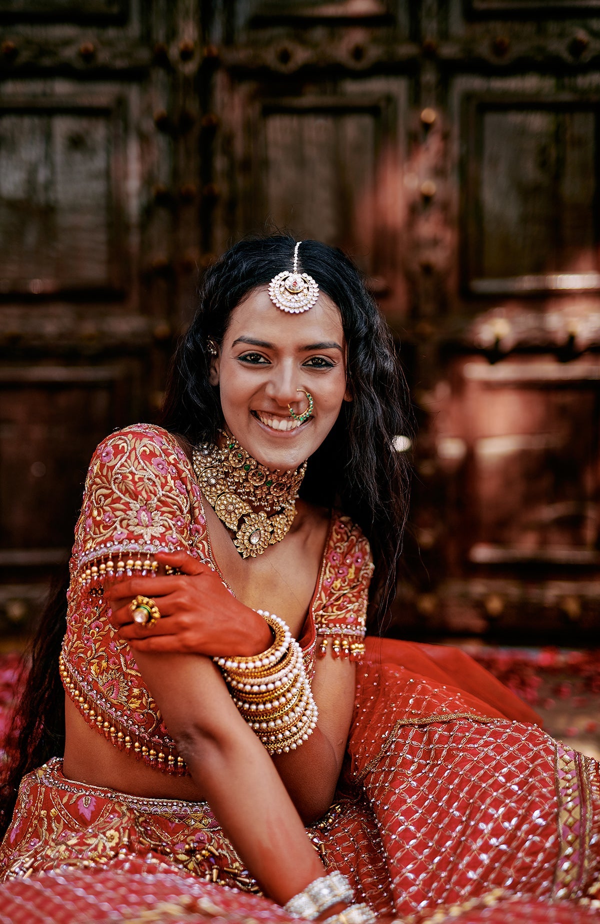 Red lehenga set with intricate pink and gold embroidery, crystal accents, tassels, and sheer dupatta.