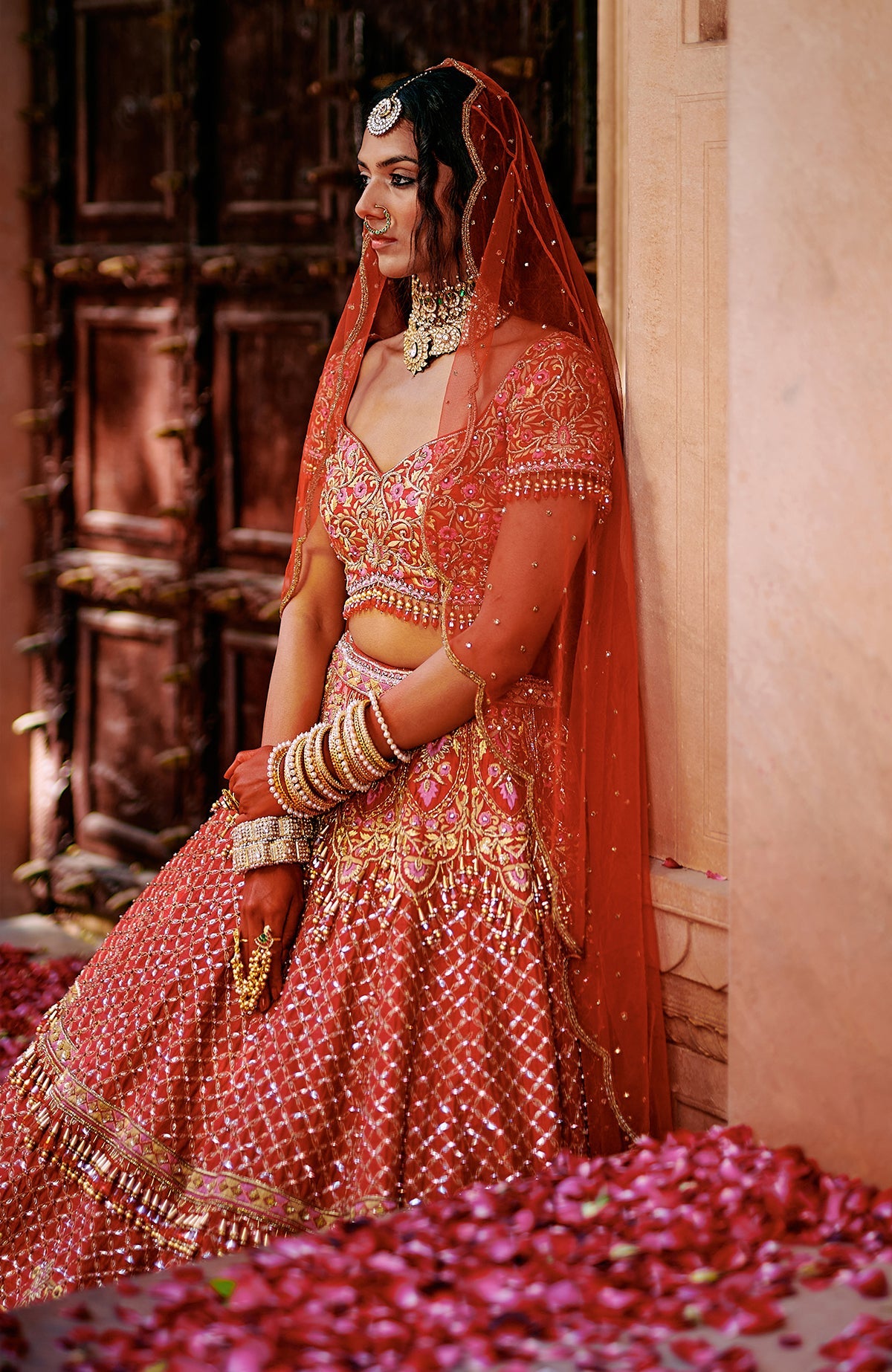Red lehenga set with gold and pink embroidery, crystal embellishments, tassels, and sheer dupatta.