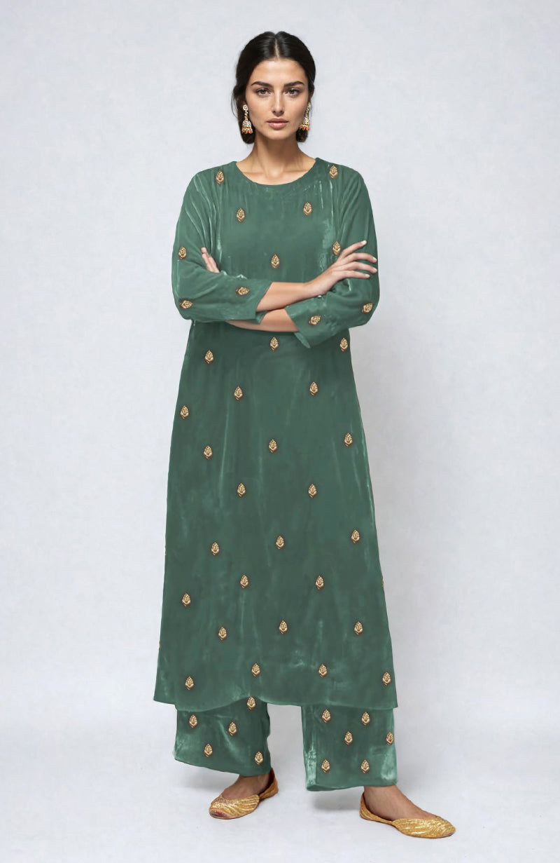 A woman models a jade green velvet kurta set with gold embroidery.