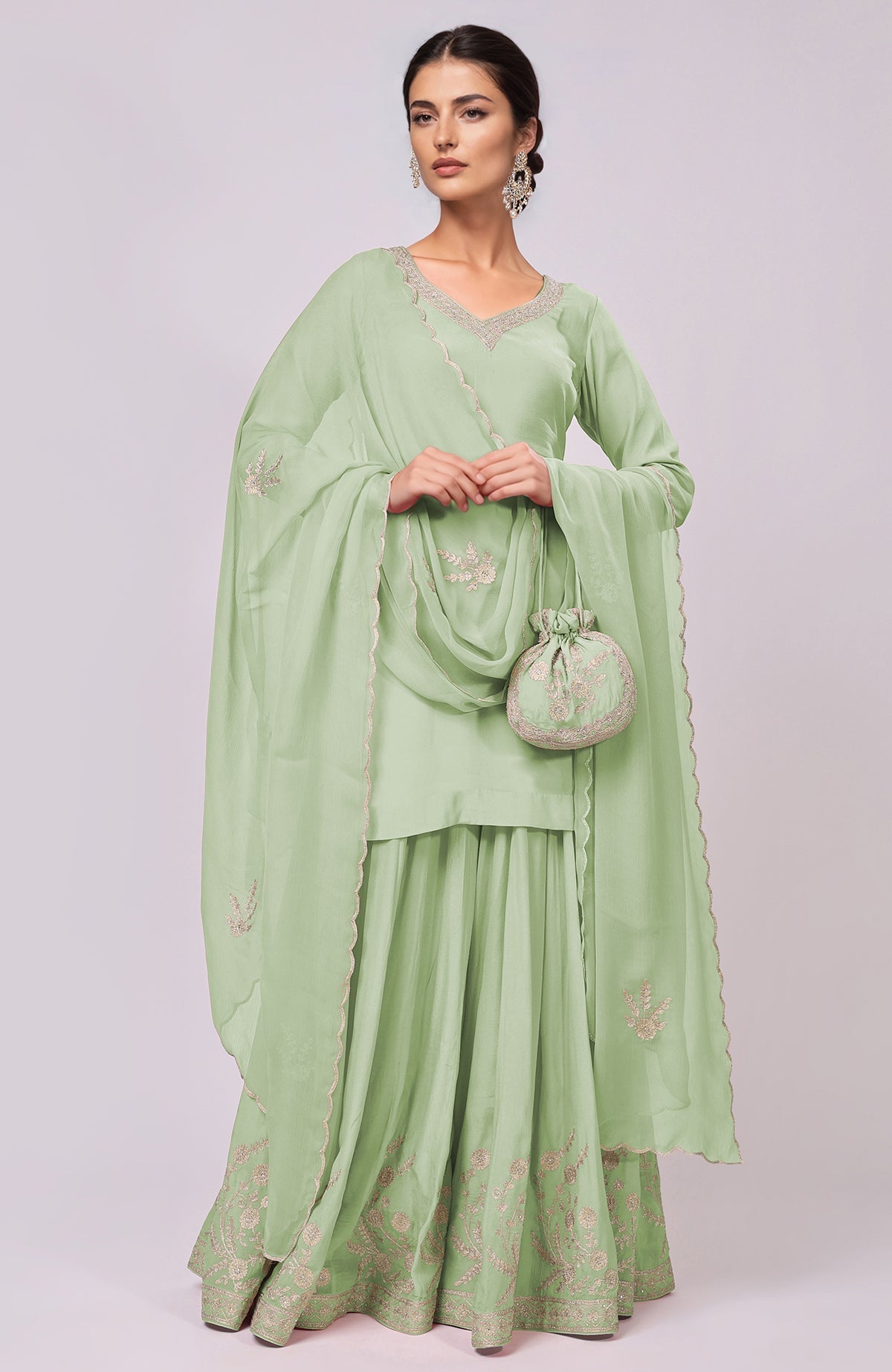 A woman models a light green sharara set with intricate embroidery and a matching potli bag.
