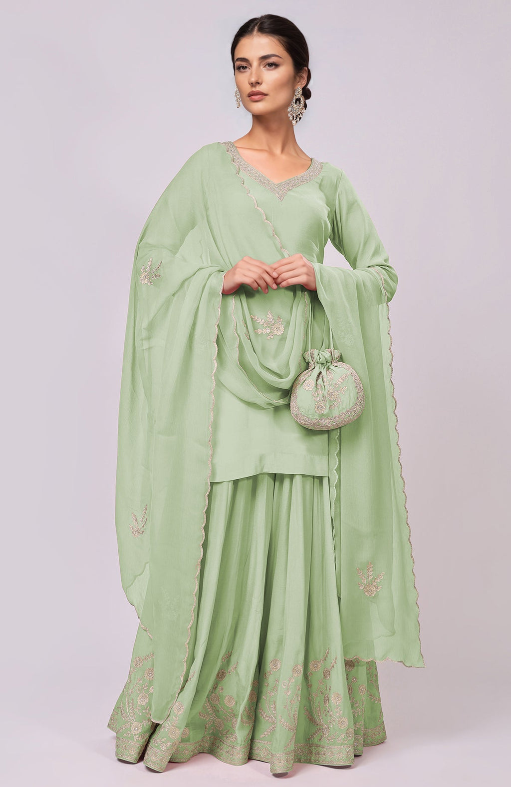 A woman models a light green Kashmiri Tilla Aari embroidered sharara set with a matching potli bag.