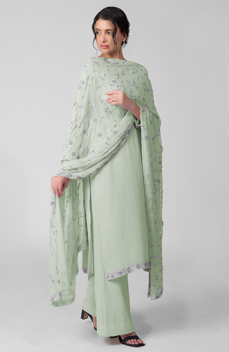 A woman models a light green kurta set with silver embroidery and black heels.