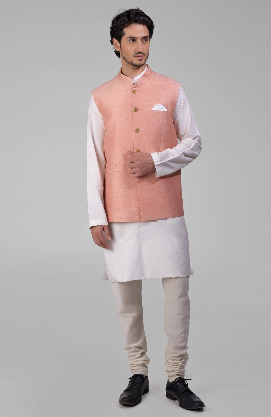 Peach raw silk waistcoat with gold buttons over a white kurta and light-colored pants.