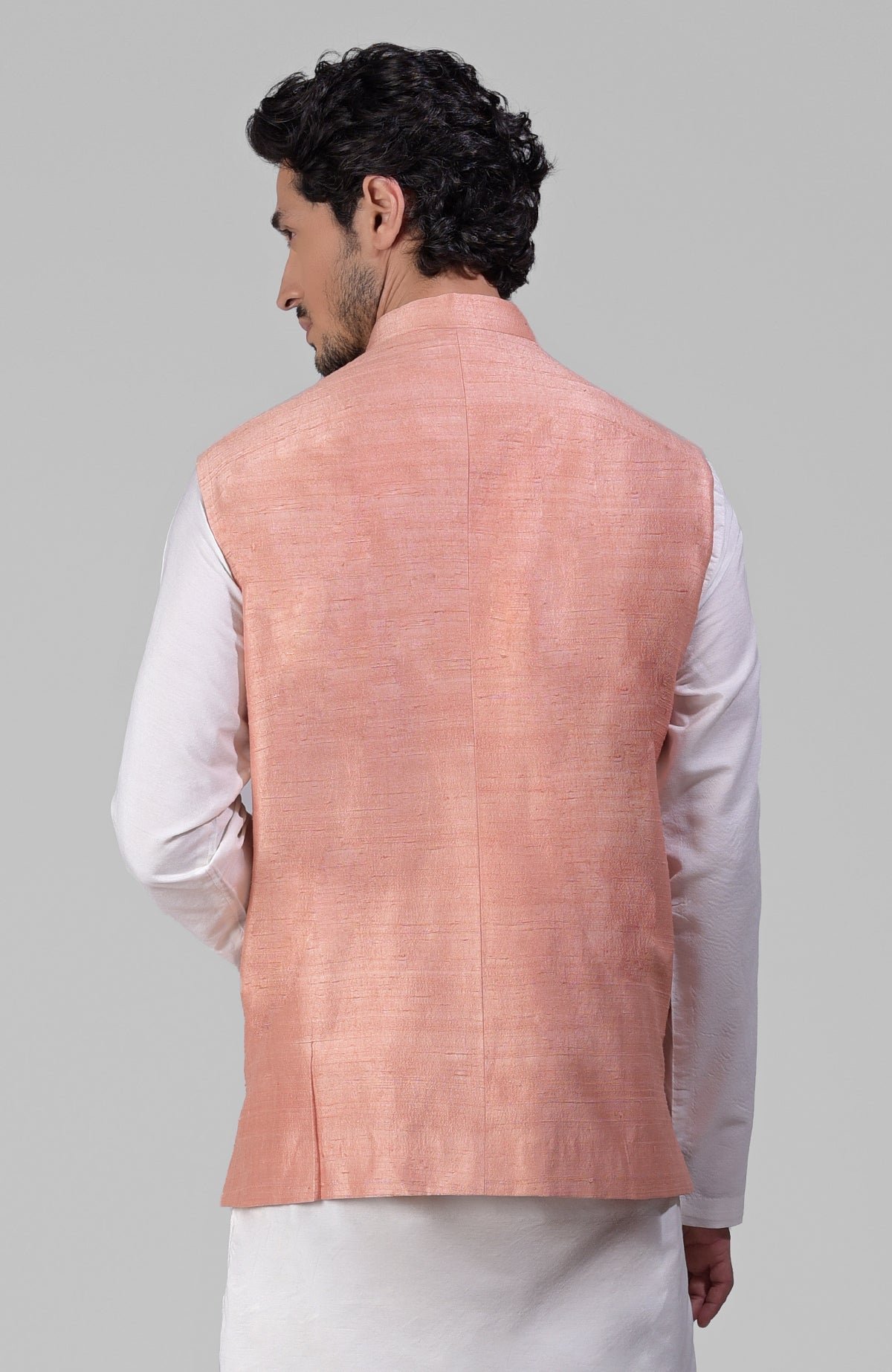 A man from behind wearing a peach raw silk waistcoat over a white kurta.