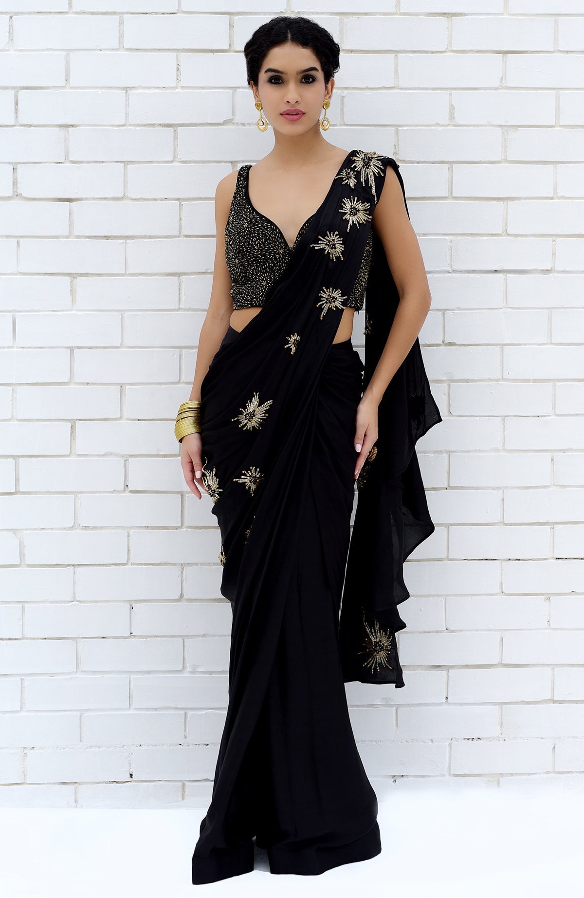 A woman models a black saree with gold starburst embroidery and a matching blouse.