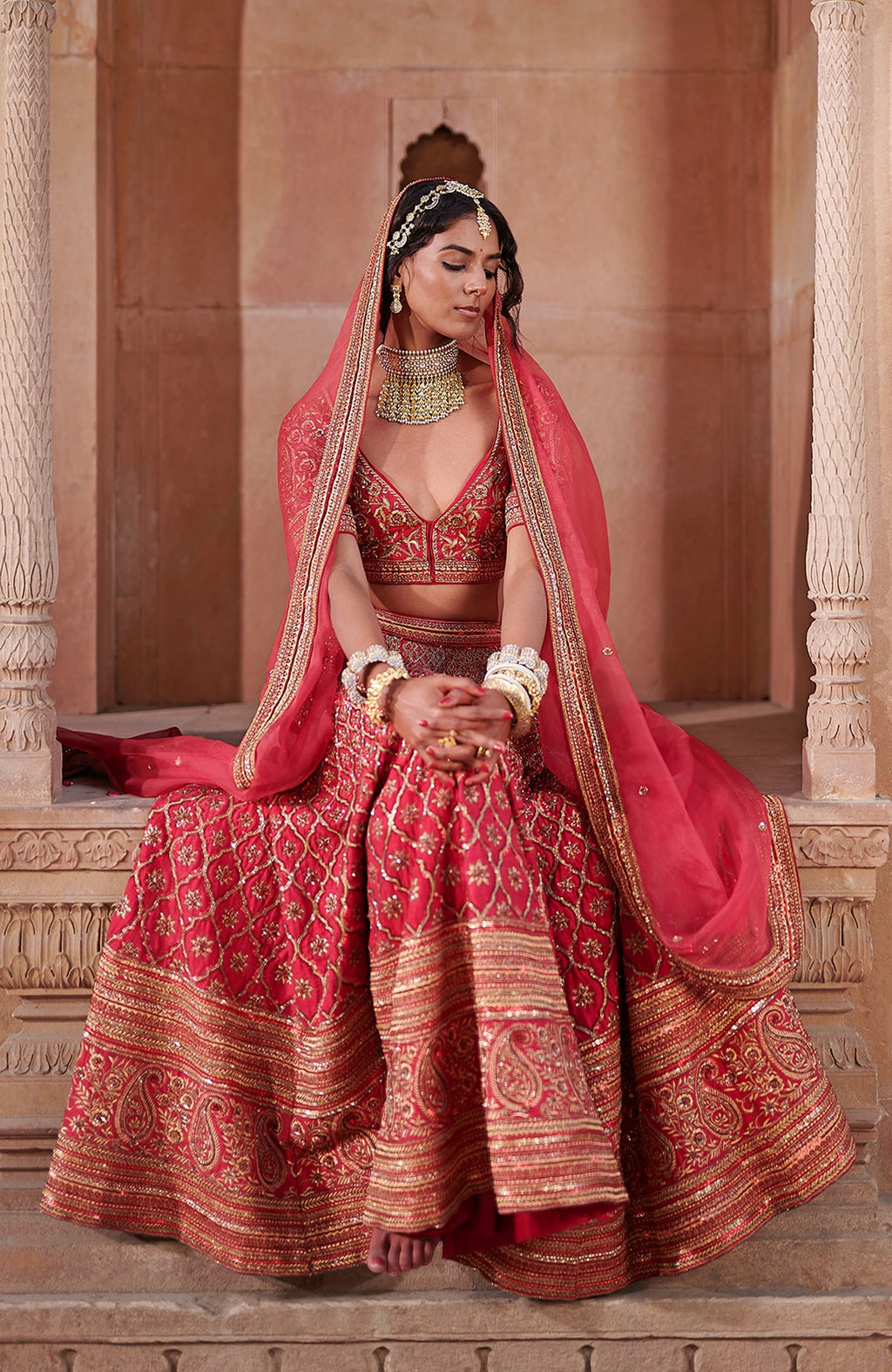 A woman in a scarlet red lehenga set with gold embroidery and jewelry.