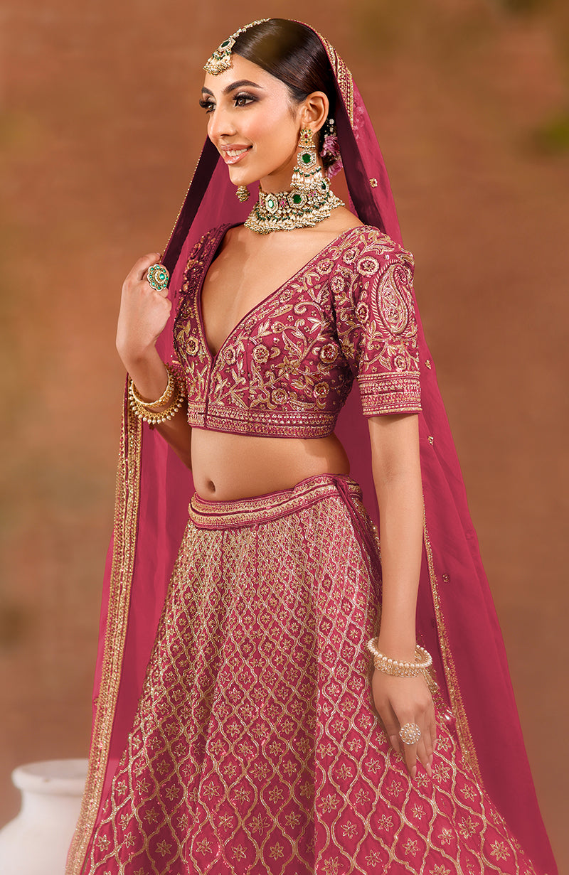 A woman in a deep rosewood lehenga set with intricate gold embroidery and jewelry.