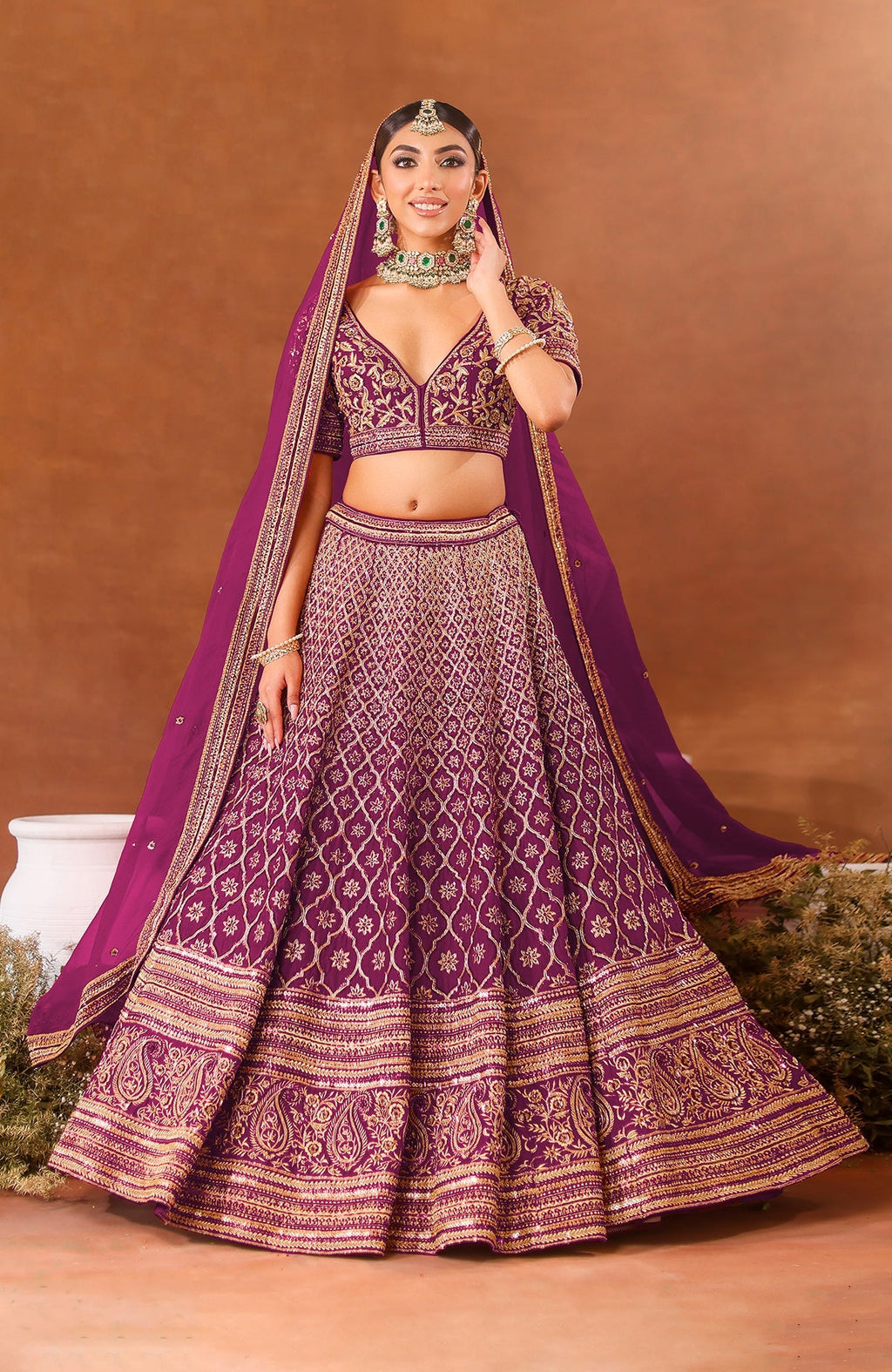 A woman models a purple wine lehenga set with gold embroidery and a matching dupatta.