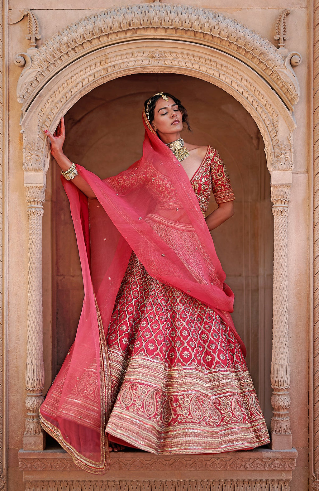 A model poses in a scarlet red lehenga set with intricate gold embroidery.